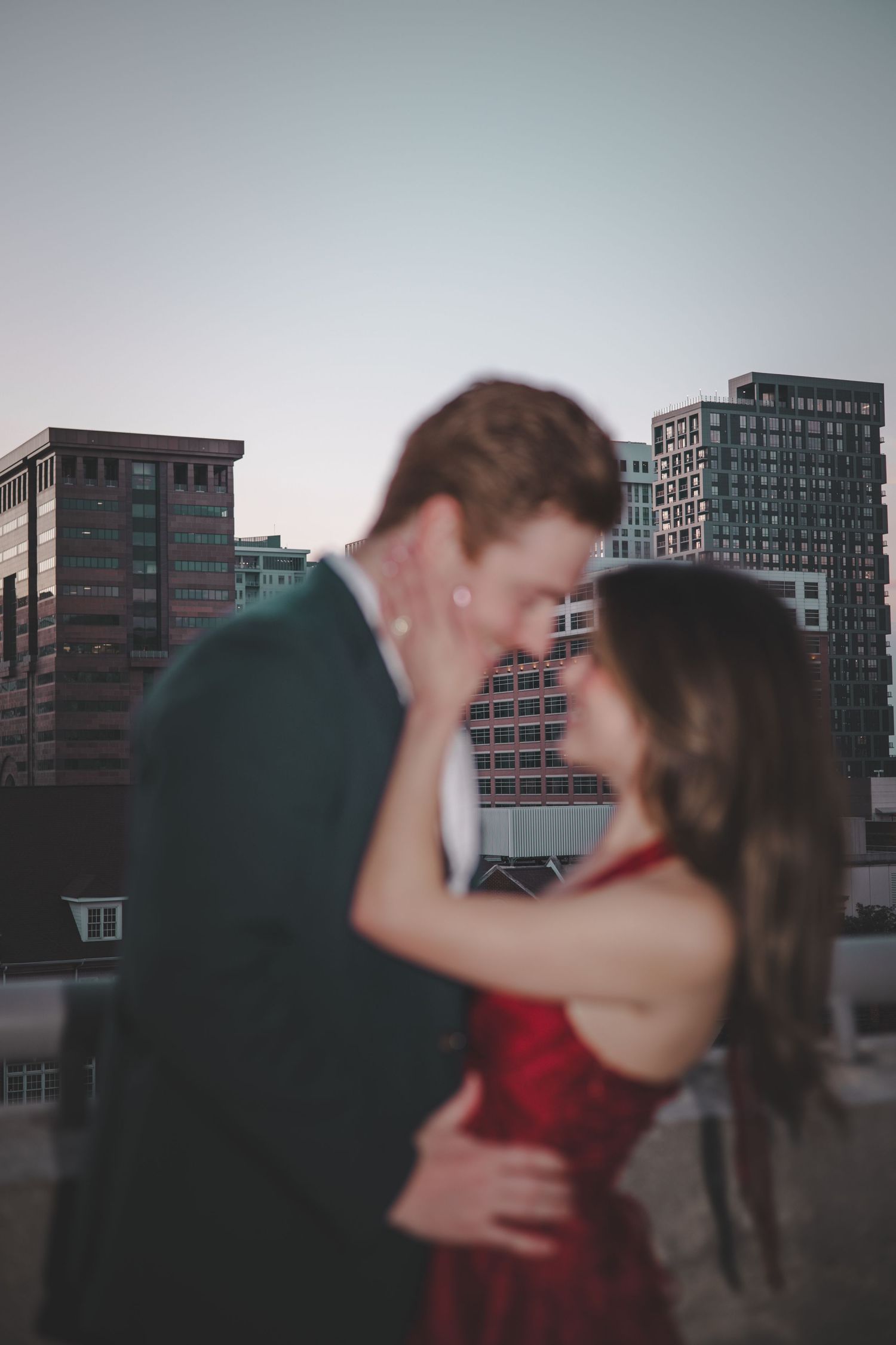 Urban rooftop engagement photos at dusk with city buildings in background.