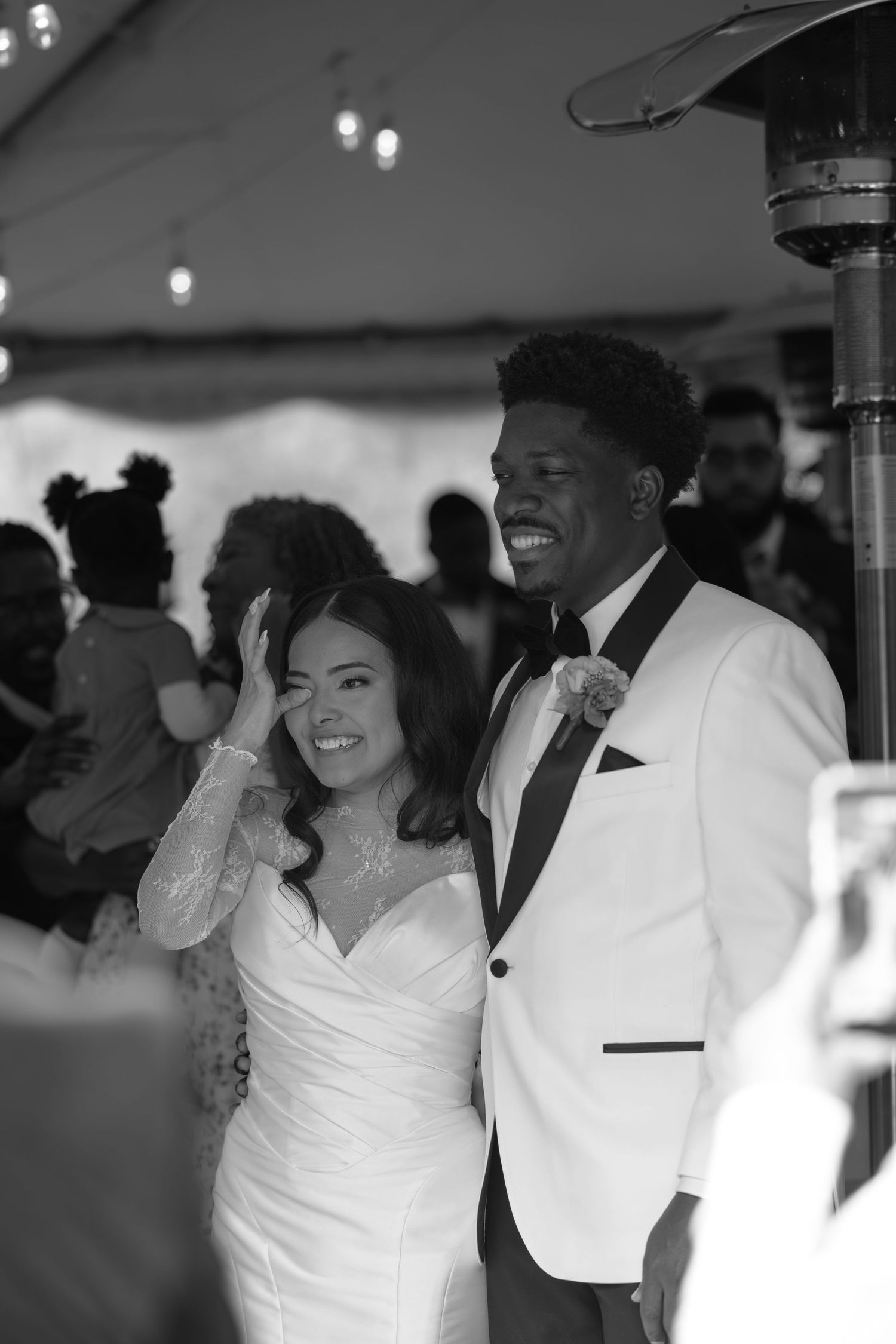 A newlywed couple shares a candid moment under tent lighting at their wedding reception.