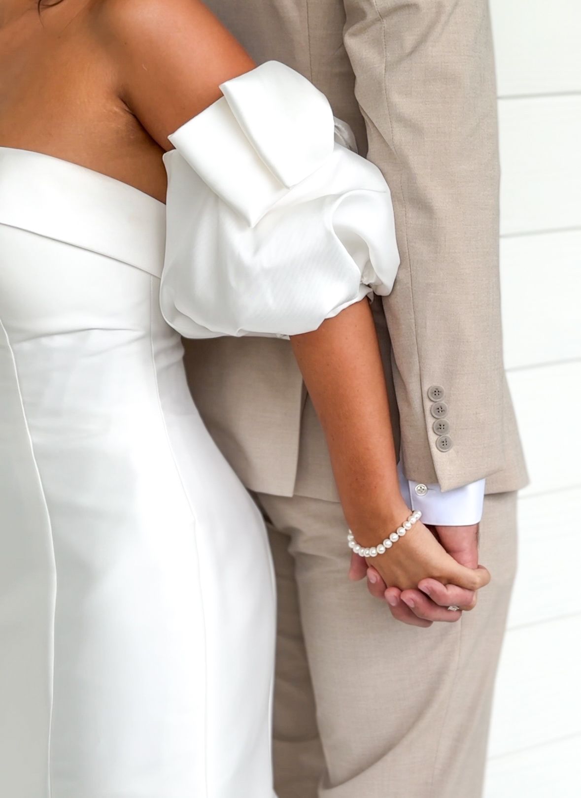 Close-up detail of a couple embracing, showing white dress and beige suit.