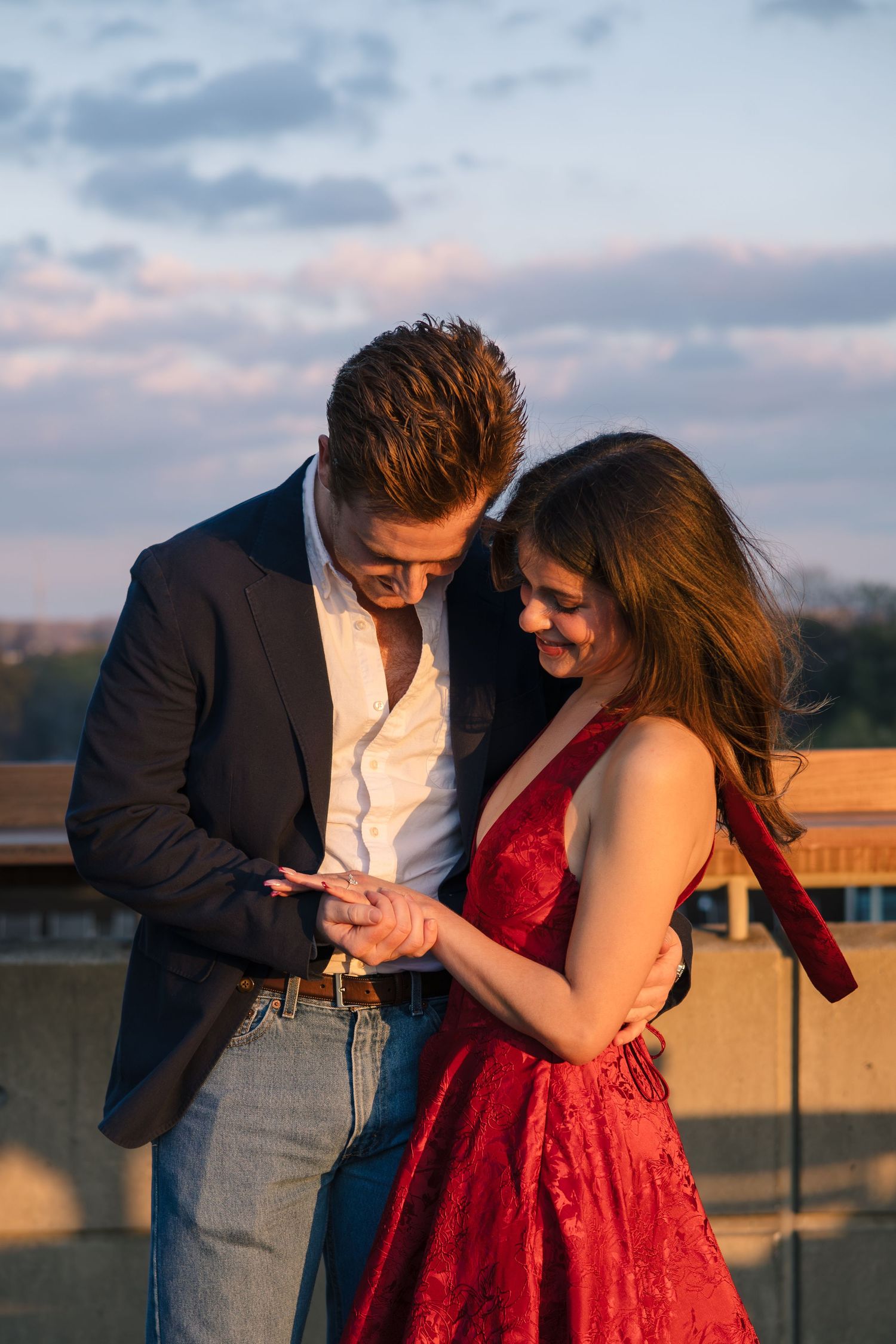 Romantic couple embracing during golden hour on a rooftop, with woman wearing red dress.