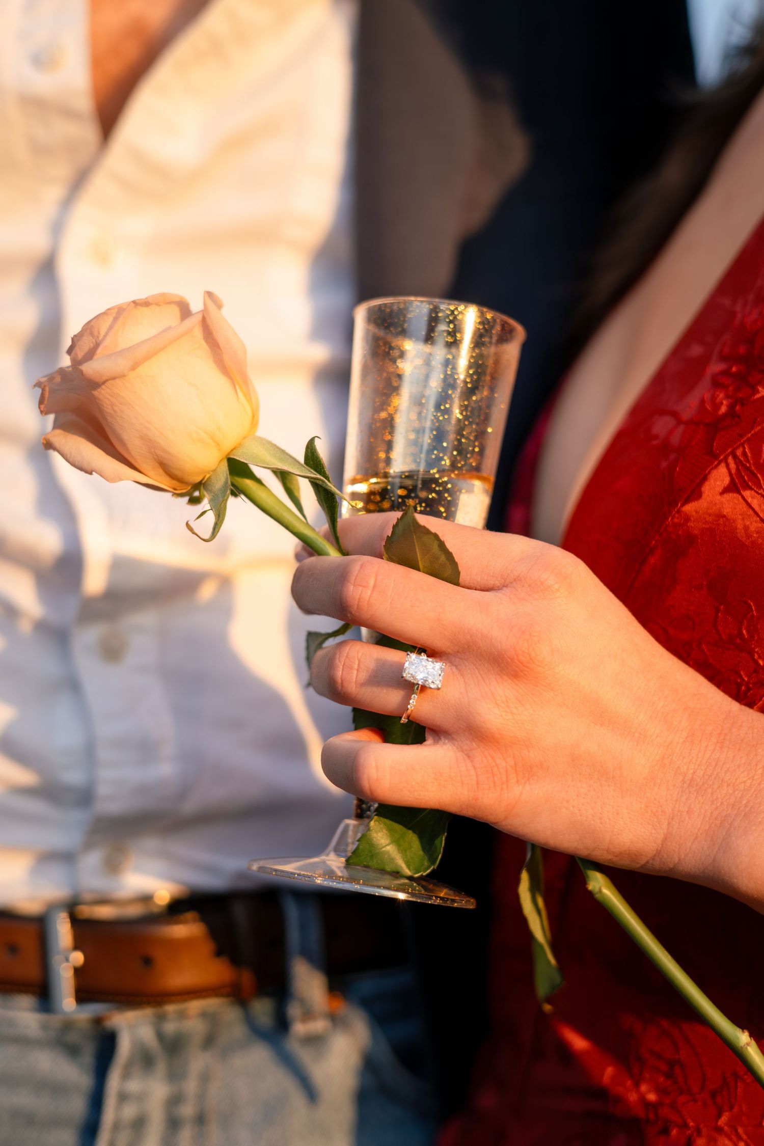 Close-up of hands holding champagne glasses and roses during romantic celebration.