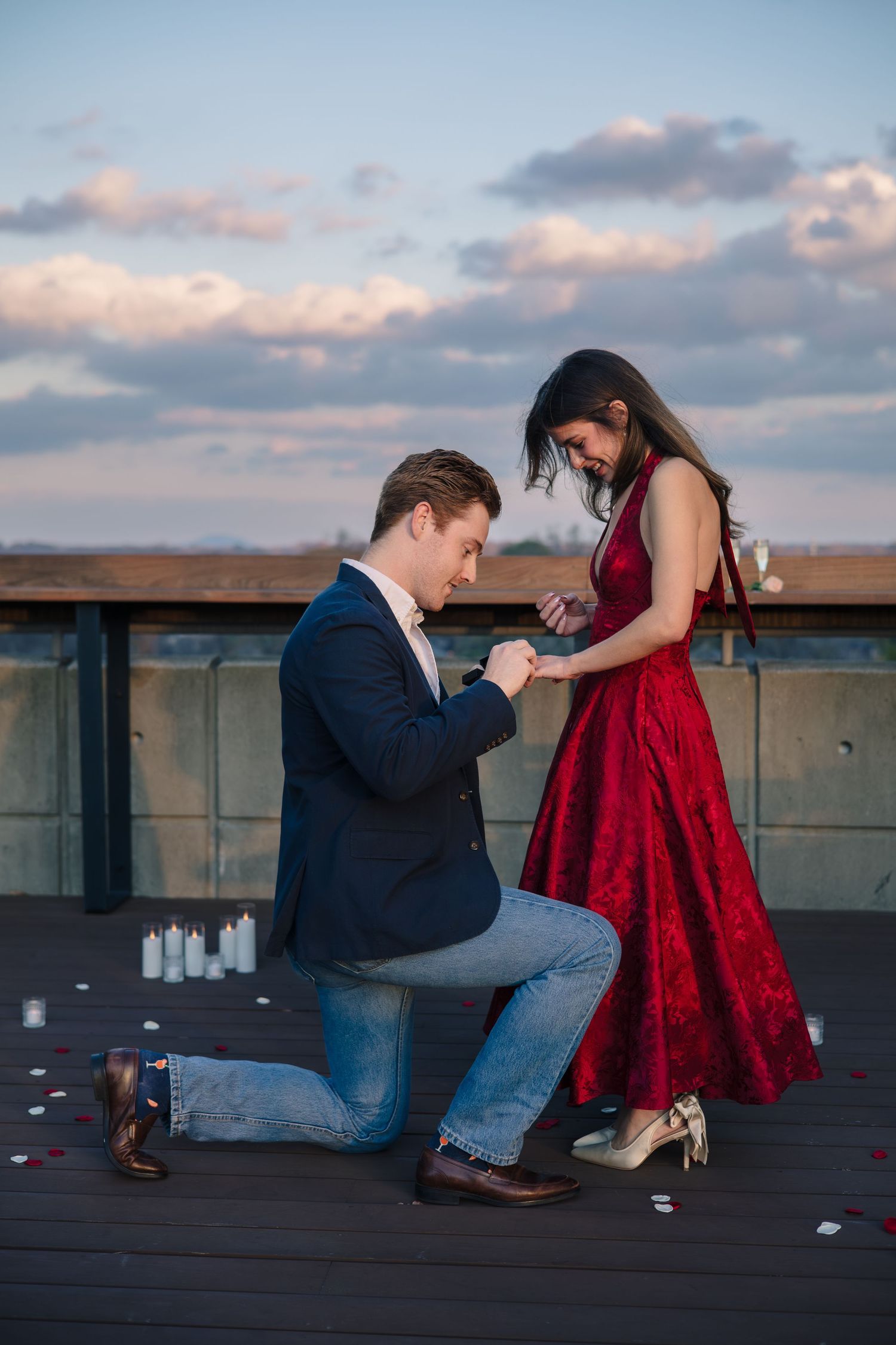 Romantic rooftop proposal scene at sunset with couple in formal attire.