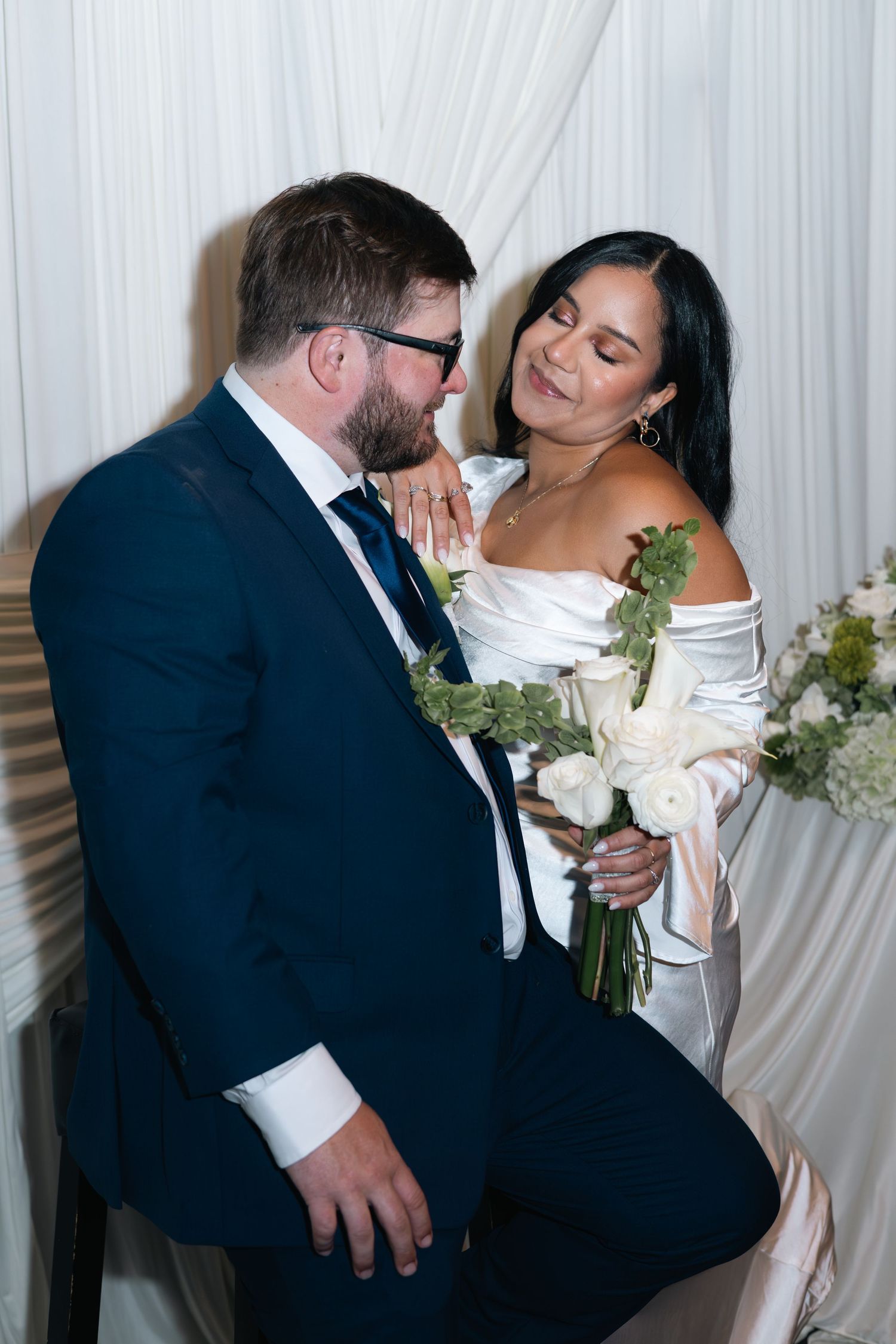 A romantic moment between newlyweds sharing an intimate pose with white roses and elegant wedding attire.