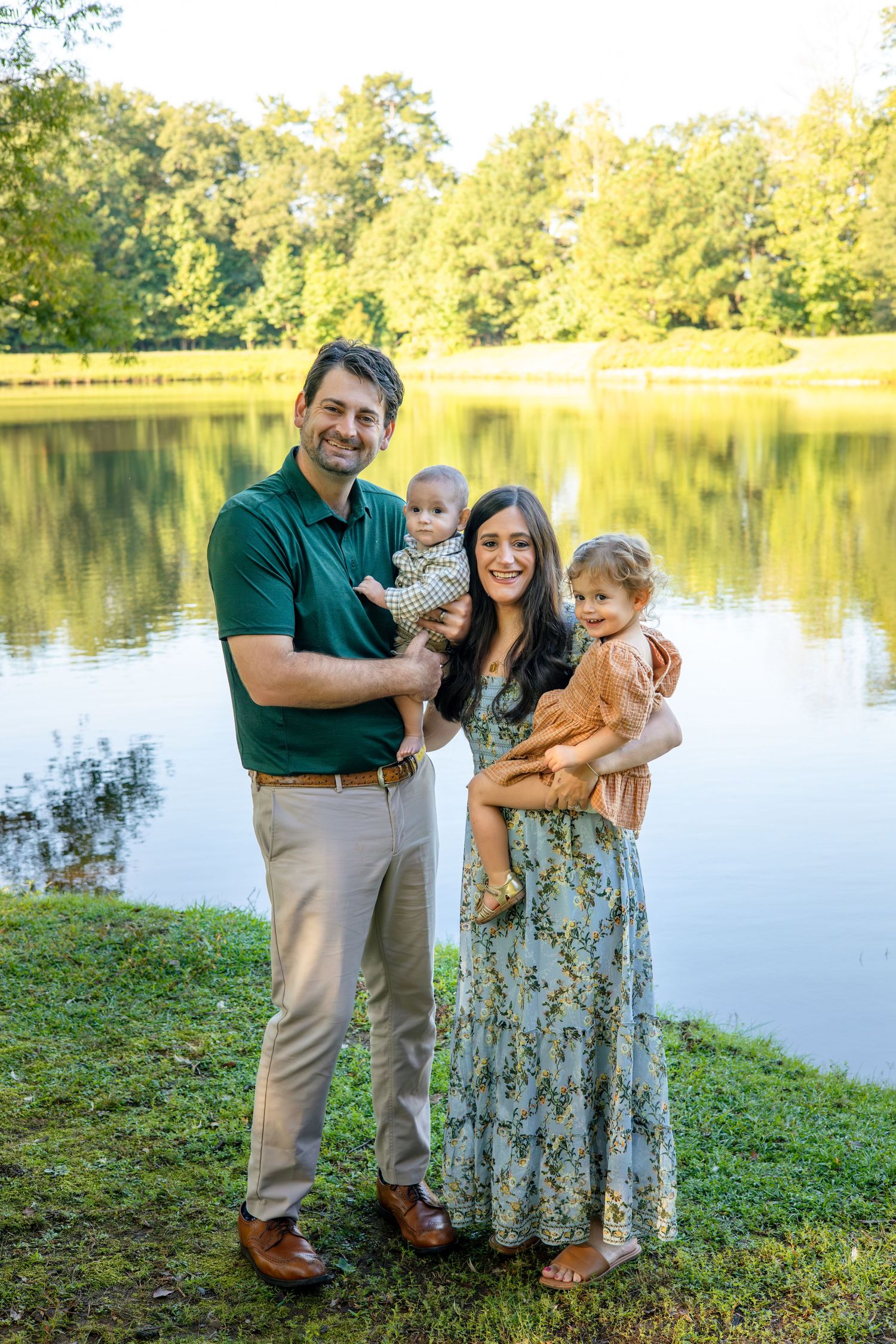 Family enjoying a sunny afternoon by a serene lake with trees reflecting in the calm water.