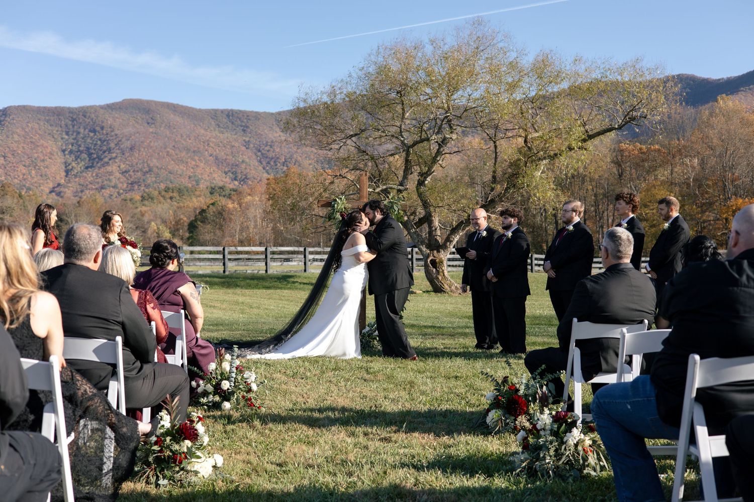 Panoramic view of an outdoor mountain wedding ceremony with guests seated on white chairs.
