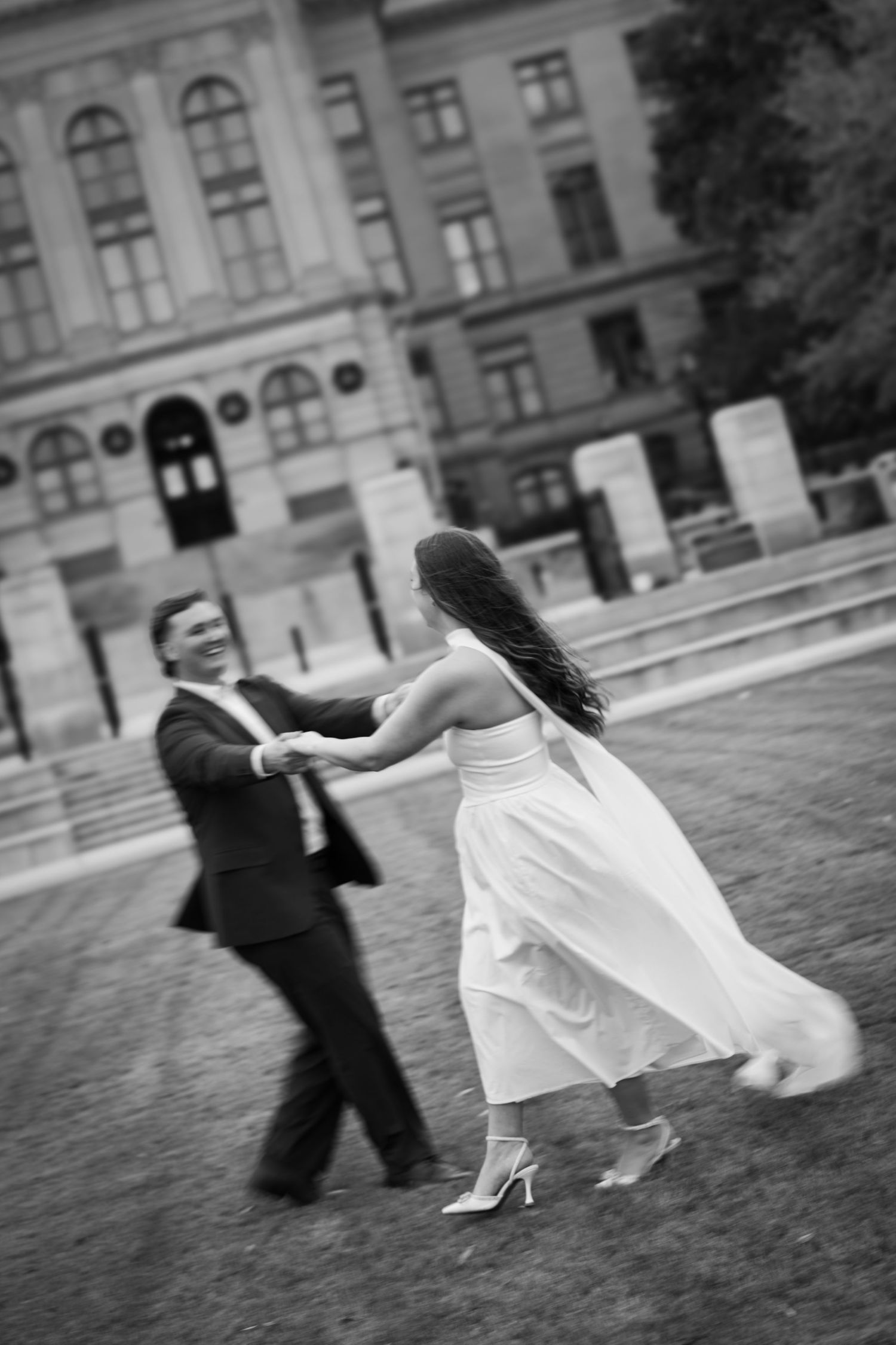 A couple dances together outdoors in black and white, her white dress flowing with movement.