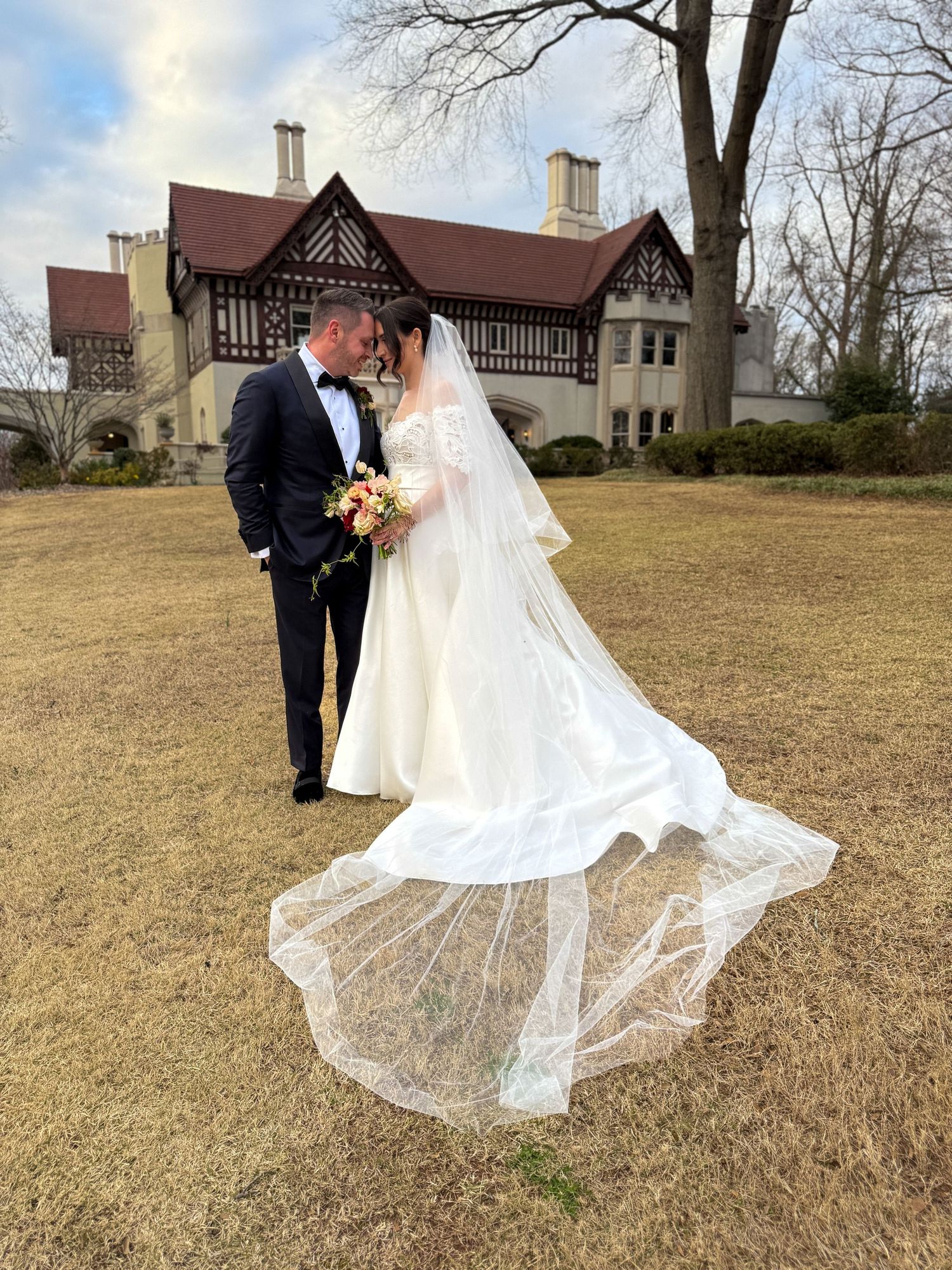 Wedding couple poses in an open field with a historic church building in the background.