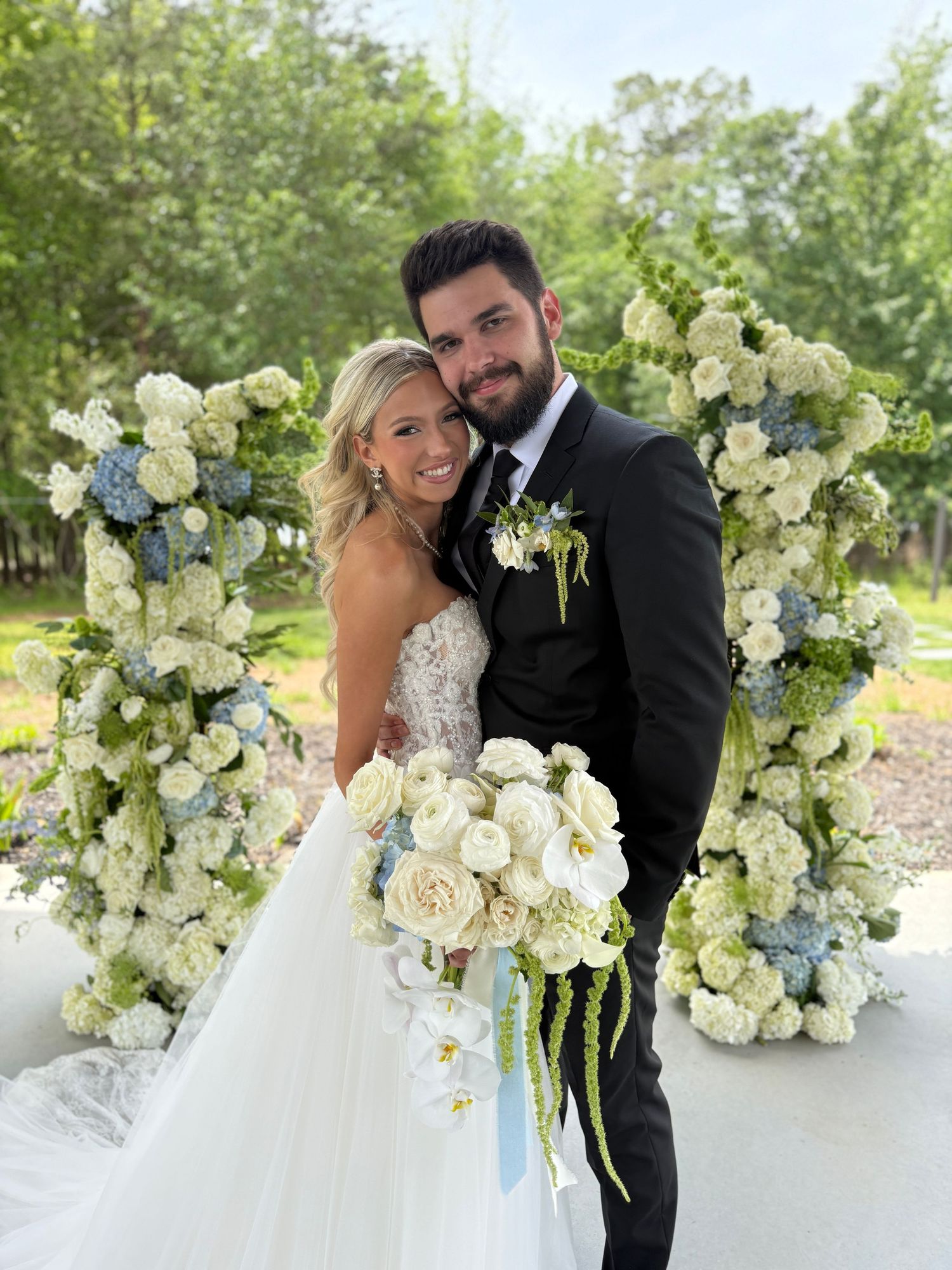 Elegant white floral arrangements with roses and hydrangeas decorate an outdoor wedding ceremony space.