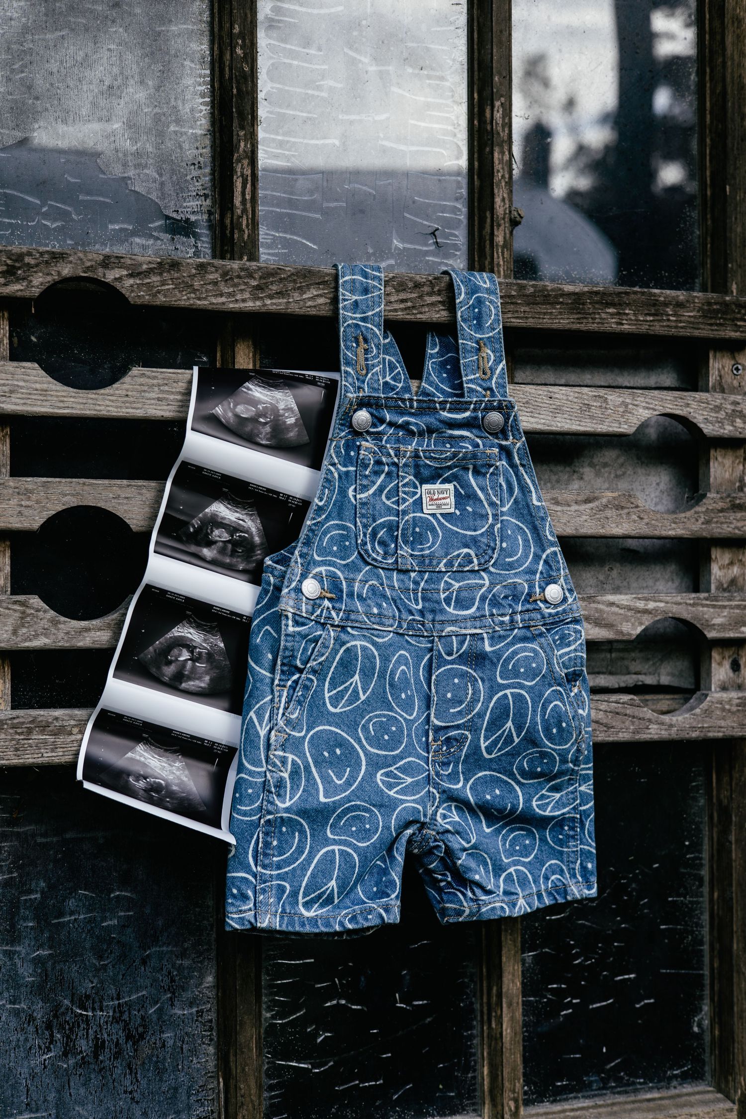 Blue patterned baby overalls displayed with ultrasound photos on a rustic wooden surface.