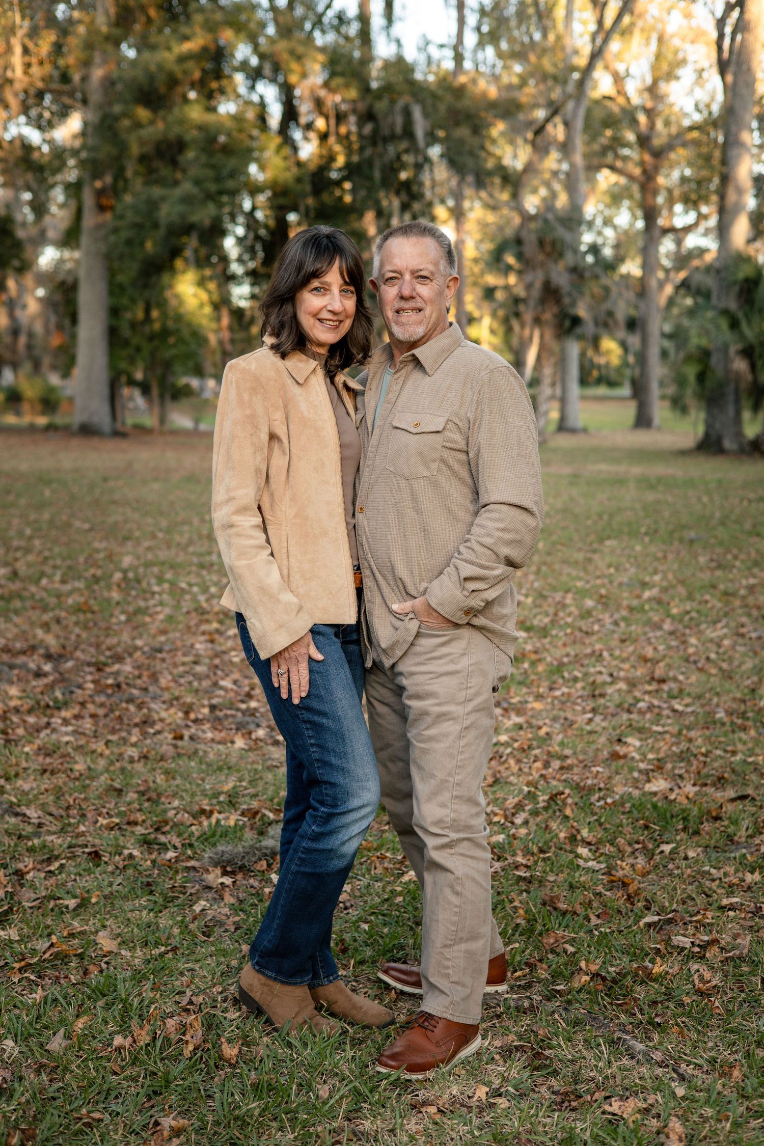 Couple in casual fall attire embracing outdoors among autumn leaves.