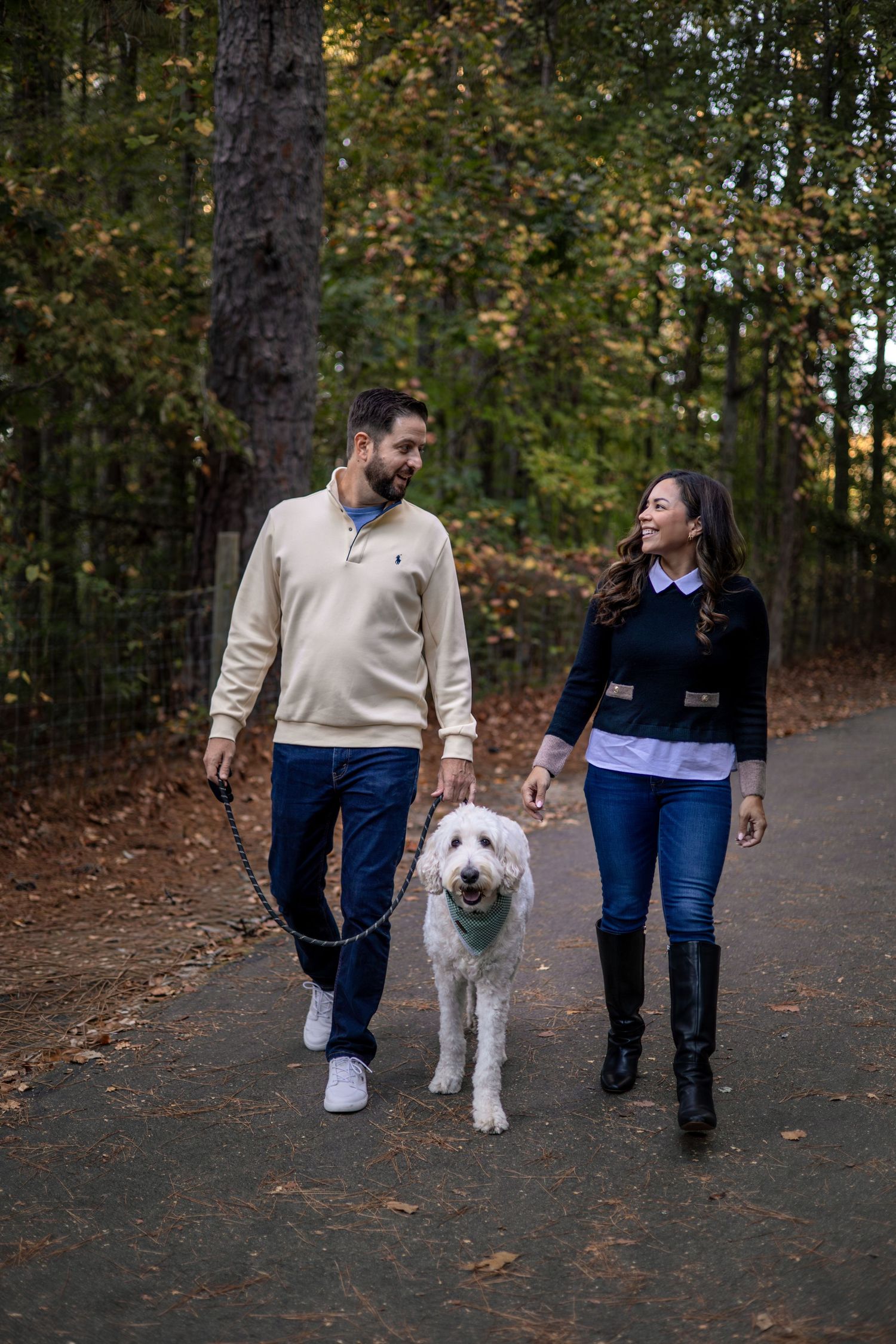 Family walking their fluffy white dog on an autumn trail through the woods.
