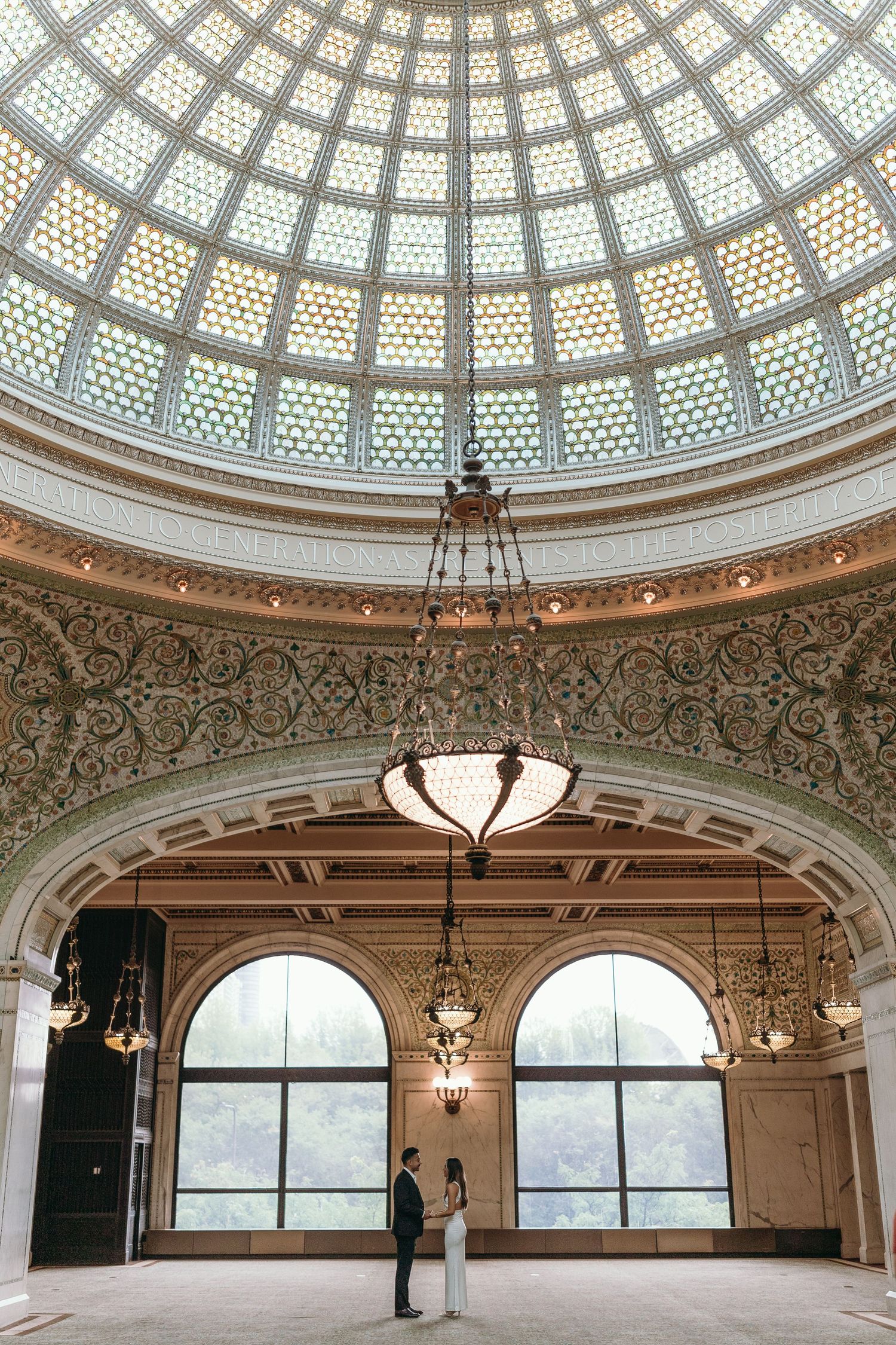 Ornate circular domed glass ceiling with intricate architectural details and elegant pendant lighting in a historic building.