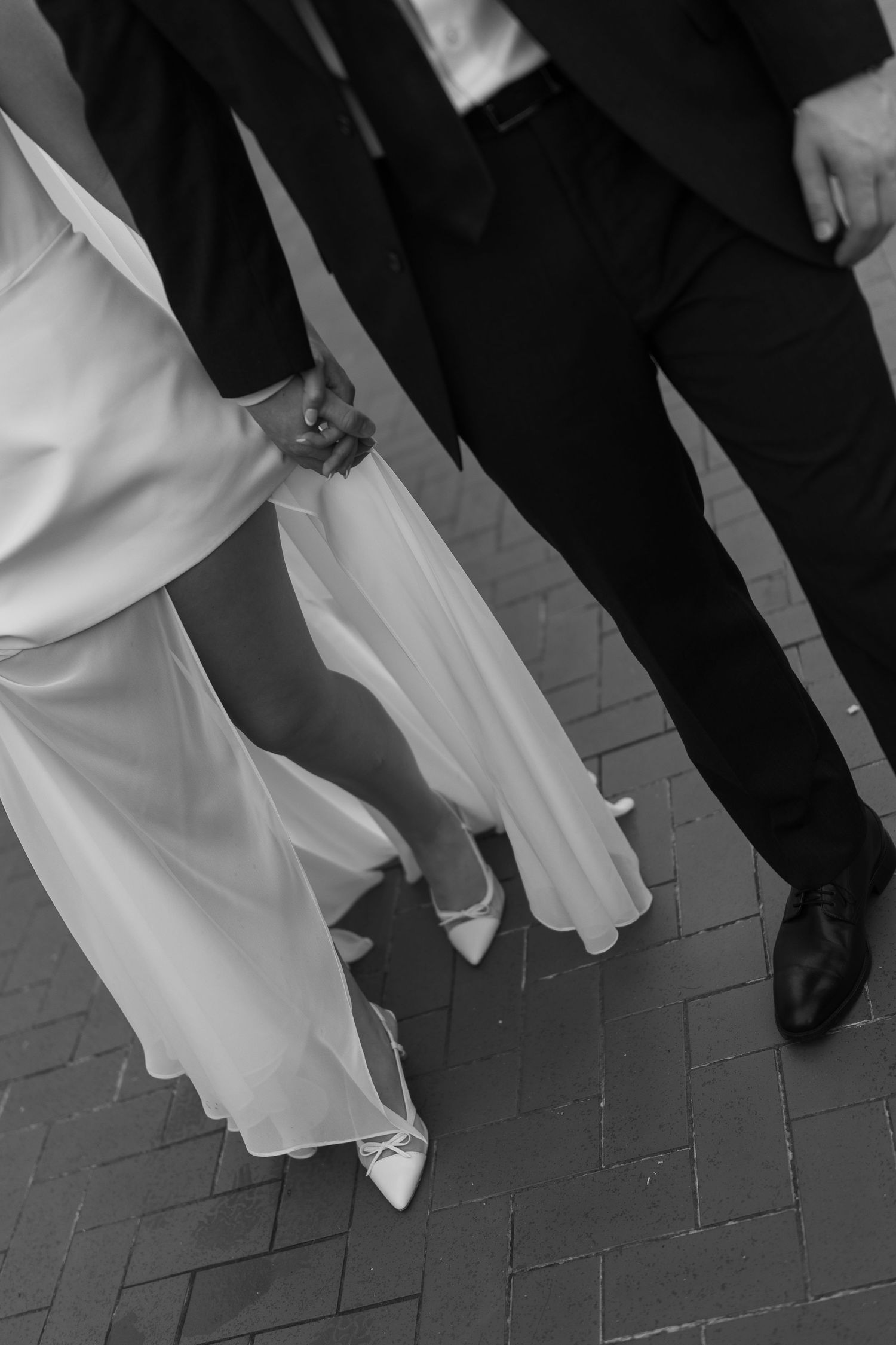 Black and white image of formal attire showing cropped legs and flowing white dresses on a patterned floor.