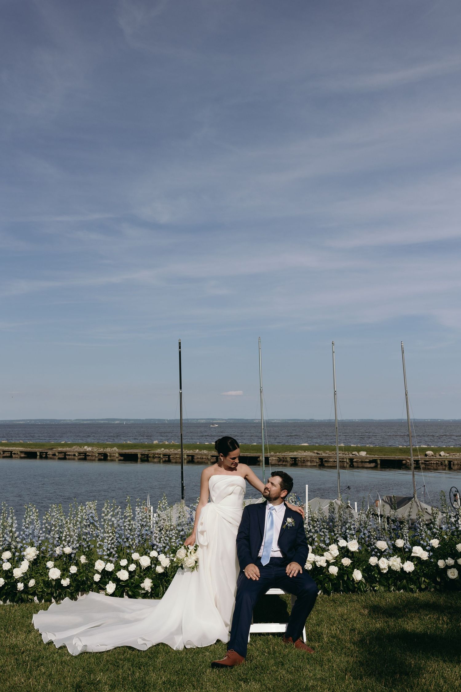 A couple shares a romantic moment in front of a waterfront garden with white flowers lakeside. Editorial chicago wedding photographer