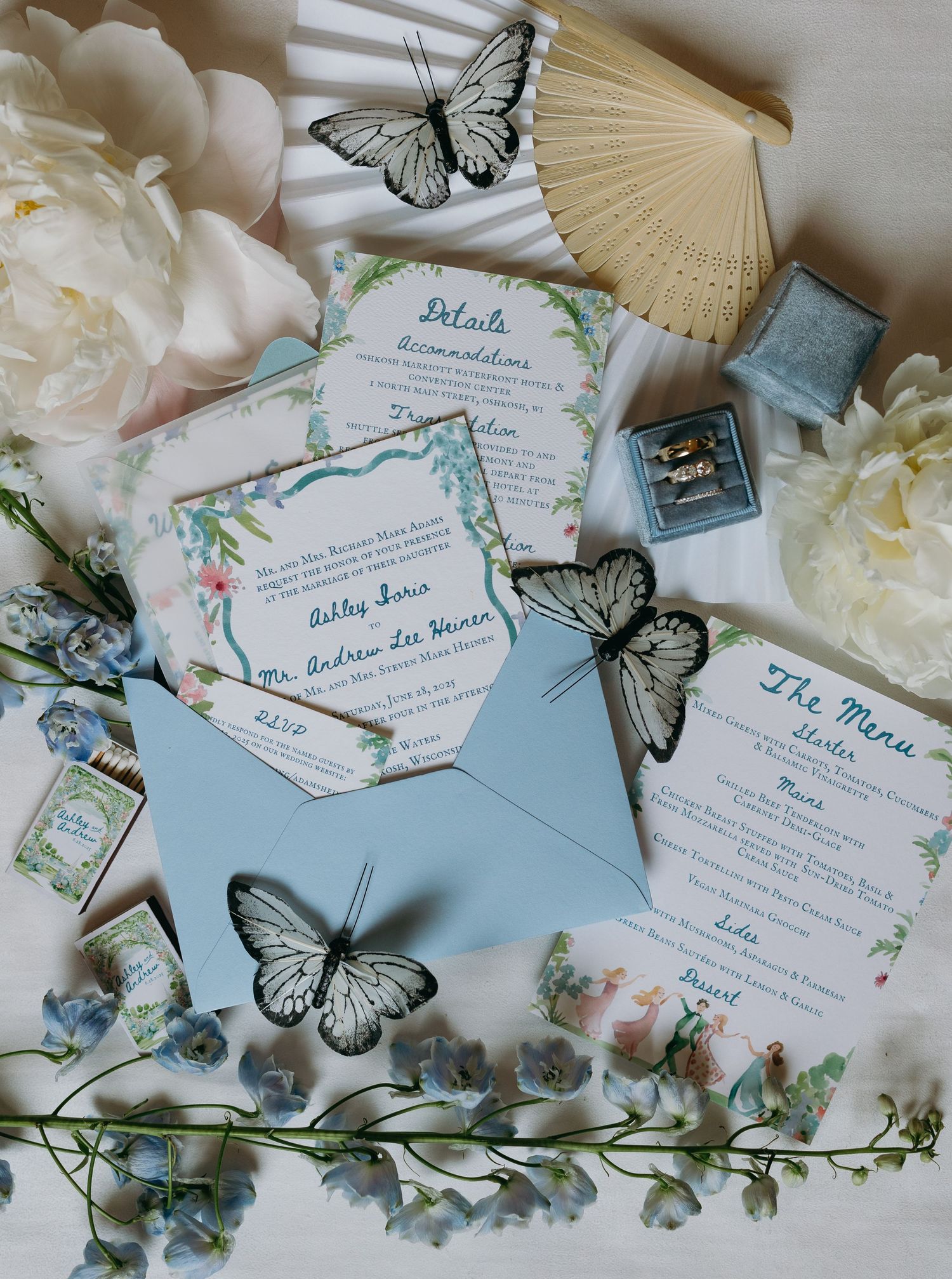 Wedding invitation suite with butterfly decorations, pastel blue envelopes, white peonies and a beige fan on light surface inspiration