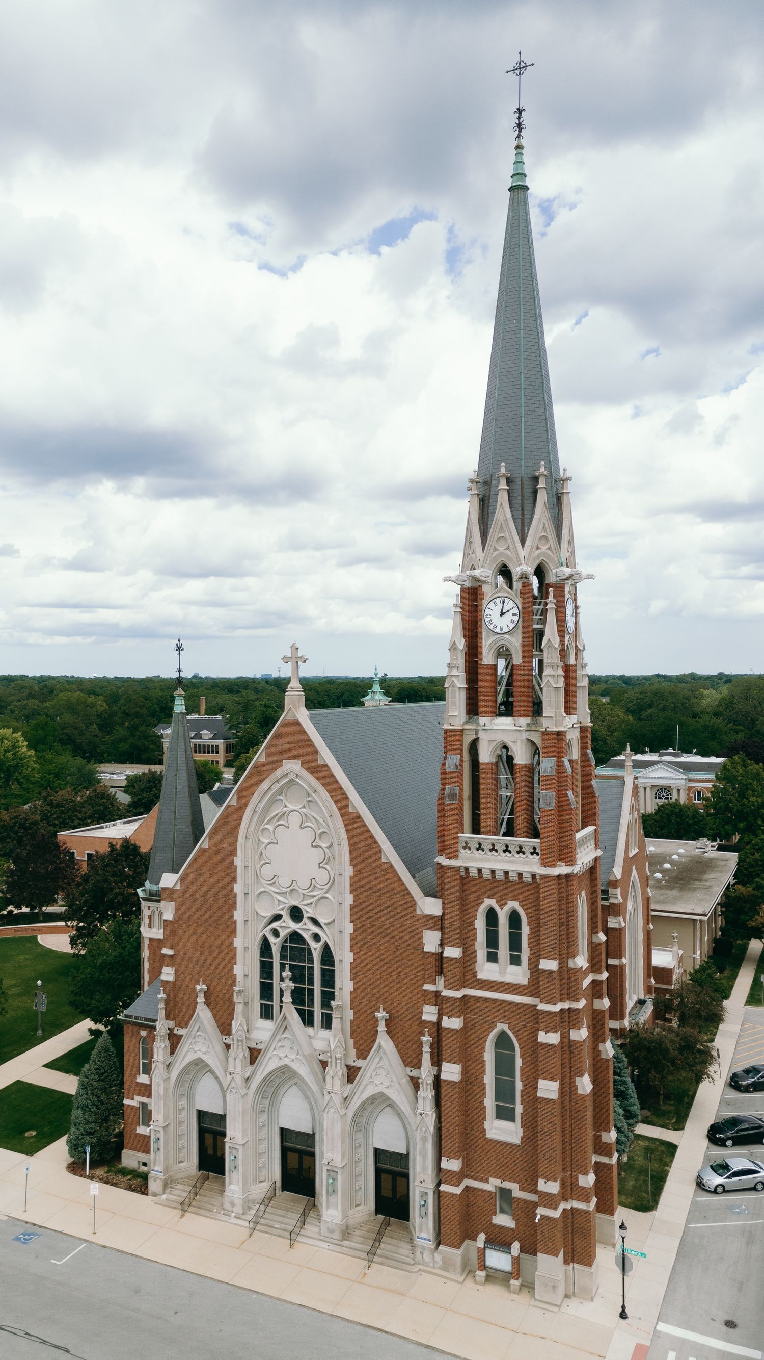 Aerial view of a Gothic revival brick church with tall spires against a cloudy sky.