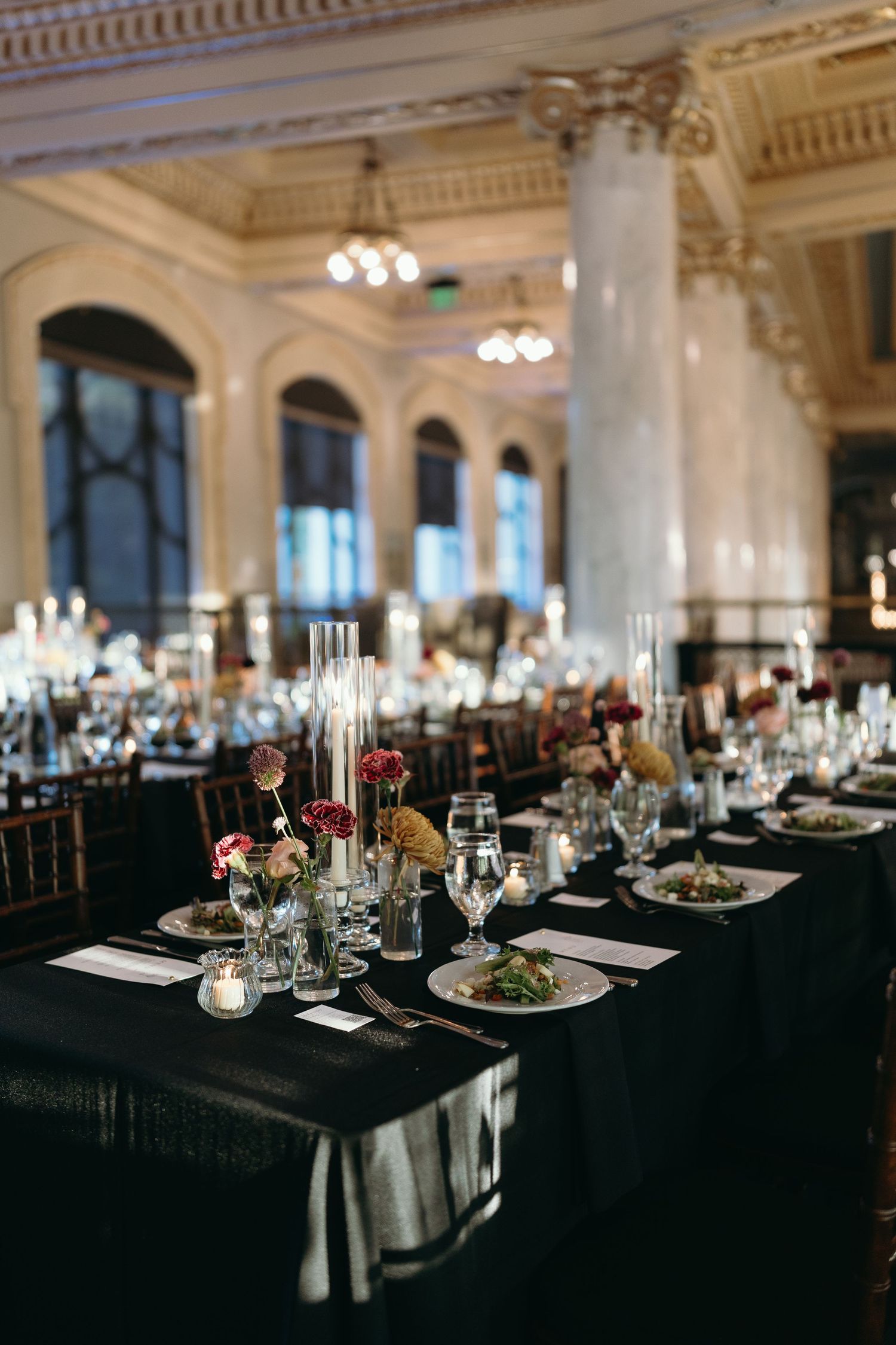 Elegant wedding reception table settings with black linens and floral centerpieces in a grand ballroom.