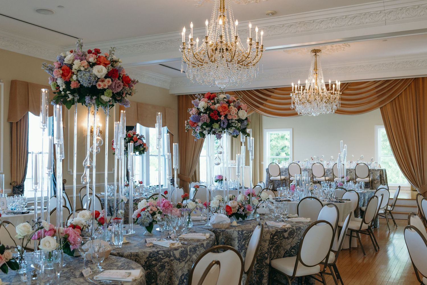 Elegant wedding reception venue with crystal chandeliers and floral centerpieces set up in a formal white ballroom.