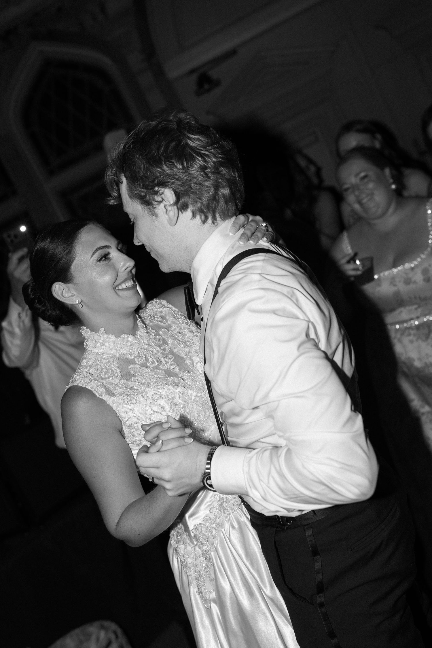 Black and white photo of a bride and groom sharing a joyful first dance at their wedding reception.