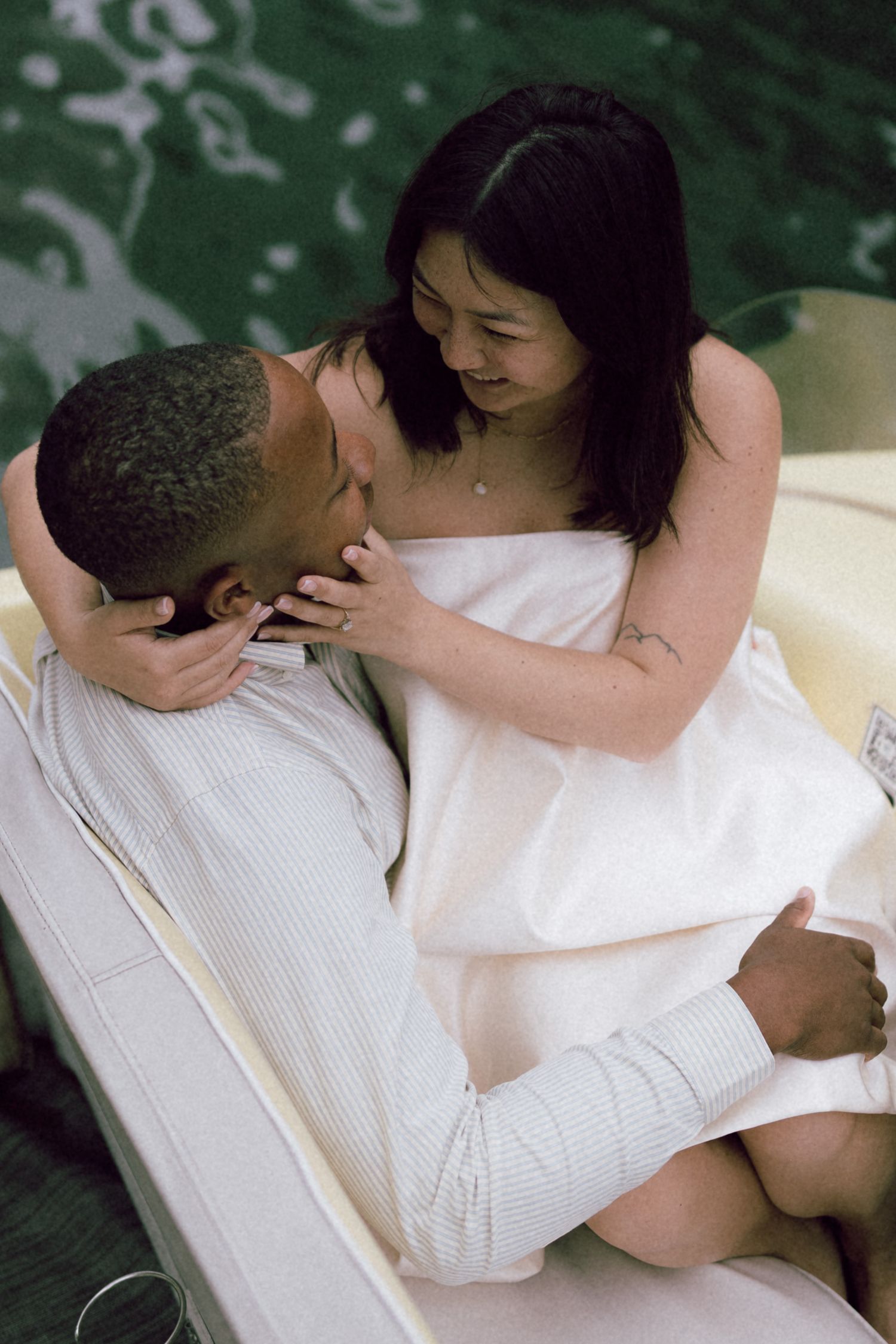 Romantic interracial couple sharing an intimate moment on a boat, woman wrapped in white towel sitting on mans lap.