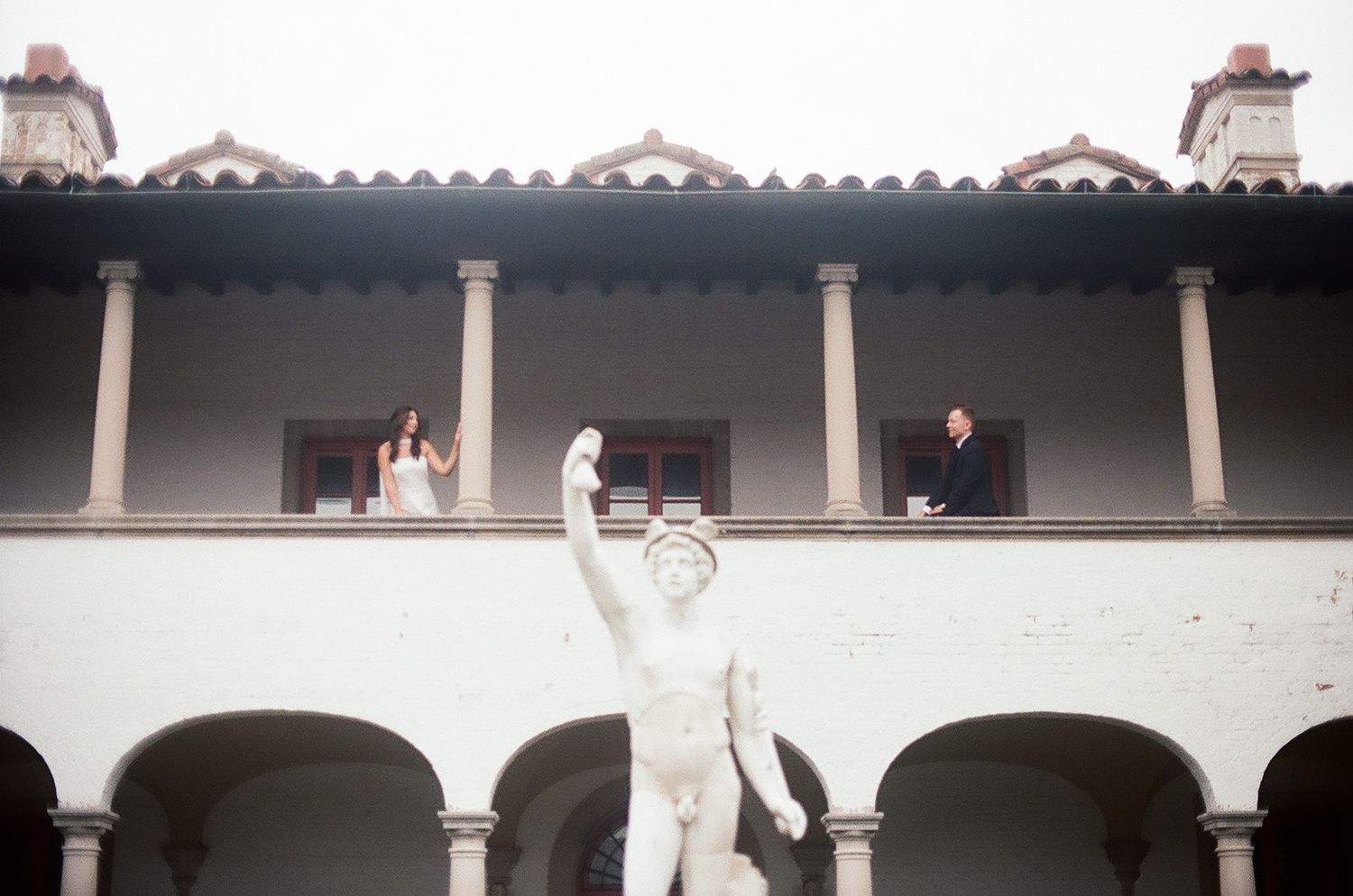 Colonial style architecture with white arches and columns along a covered walkway at Mission San Luis Rey.