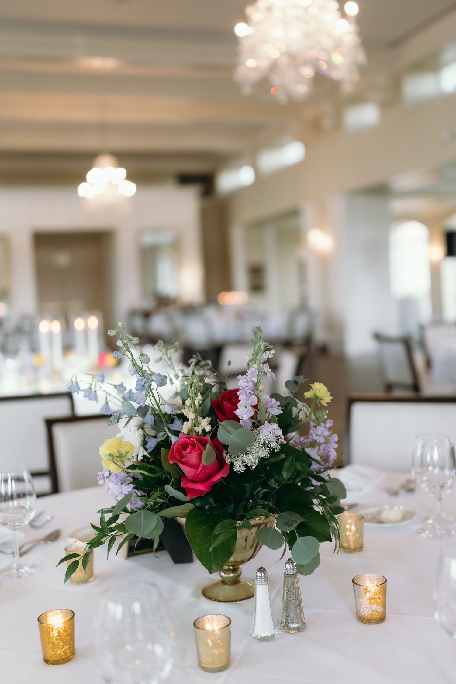 Wedding reception centerpiece with pink roses and candles on a white tablecloth.