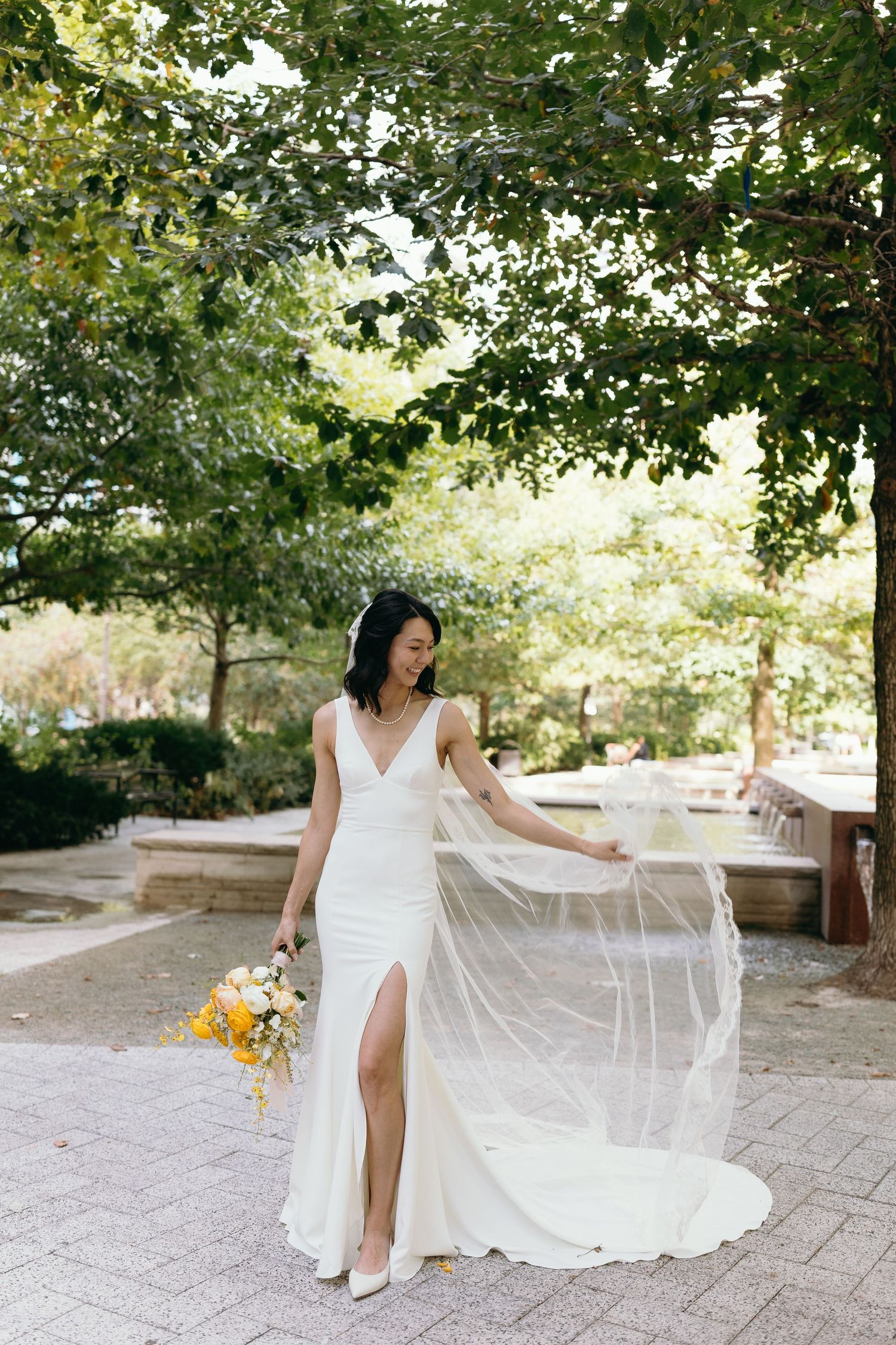 Elegant outdoor bridal portrait featuring flowing white dress and veil against natural garden backdrop.