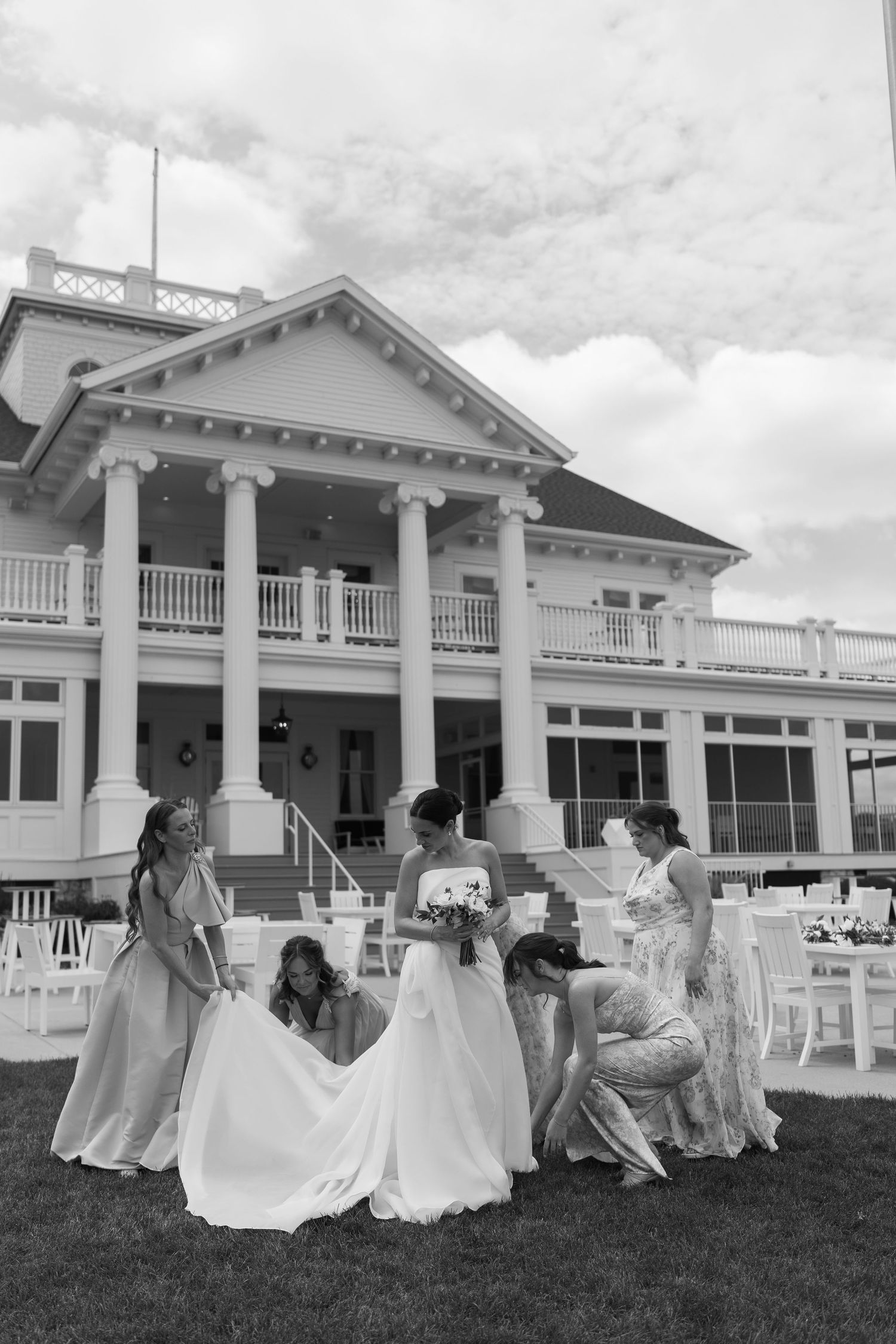 A black and white photo of a wedding party outside a stately white mansion with columns and a wraparound porch.
