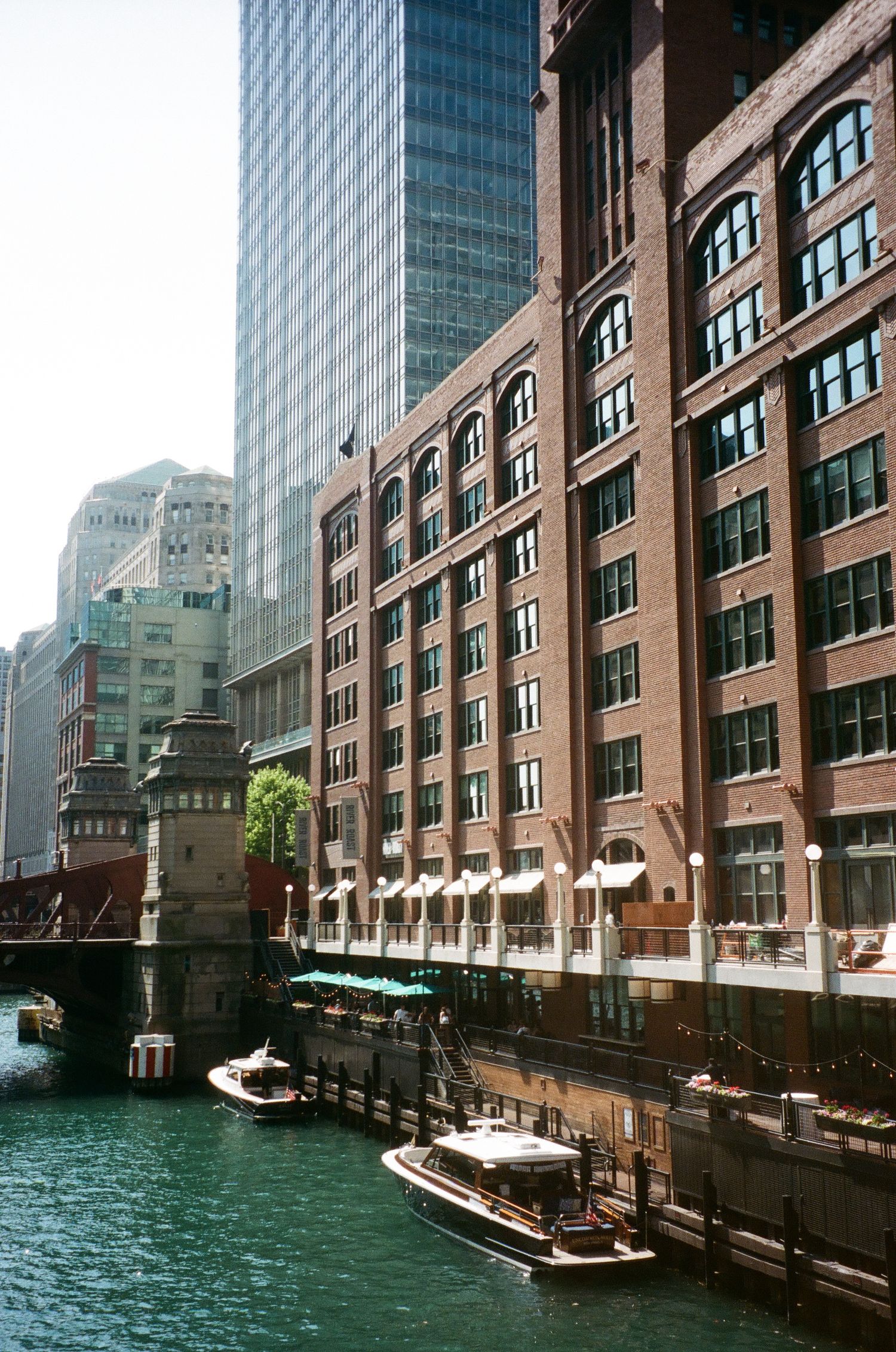 Boats cruise along the Chicago River beside a historic red brick building and modern skyscrapers on a sunny day.
