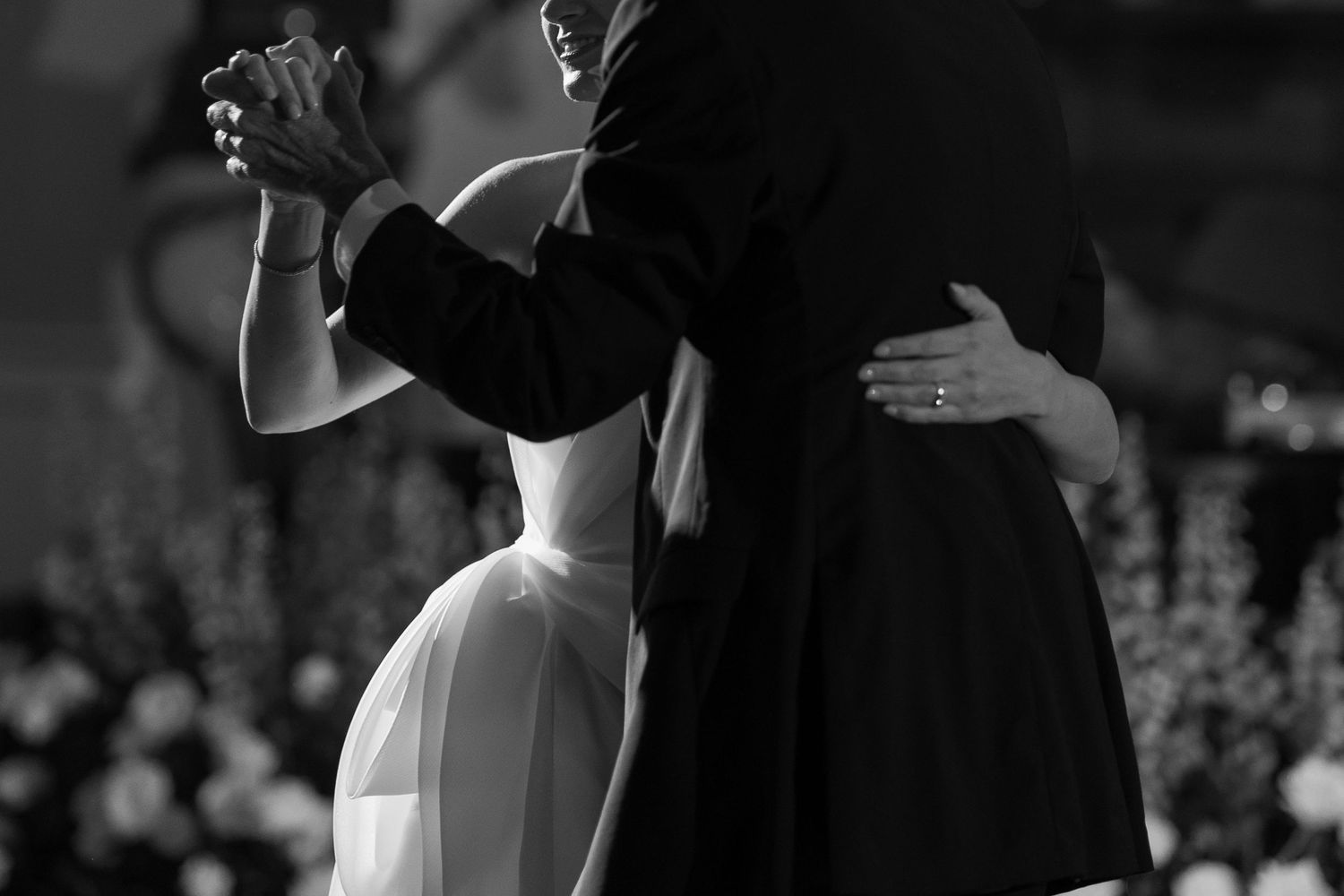 A couple elegantly dances together in formal attire, captured in black and white with dramatic lighting and contrast.
