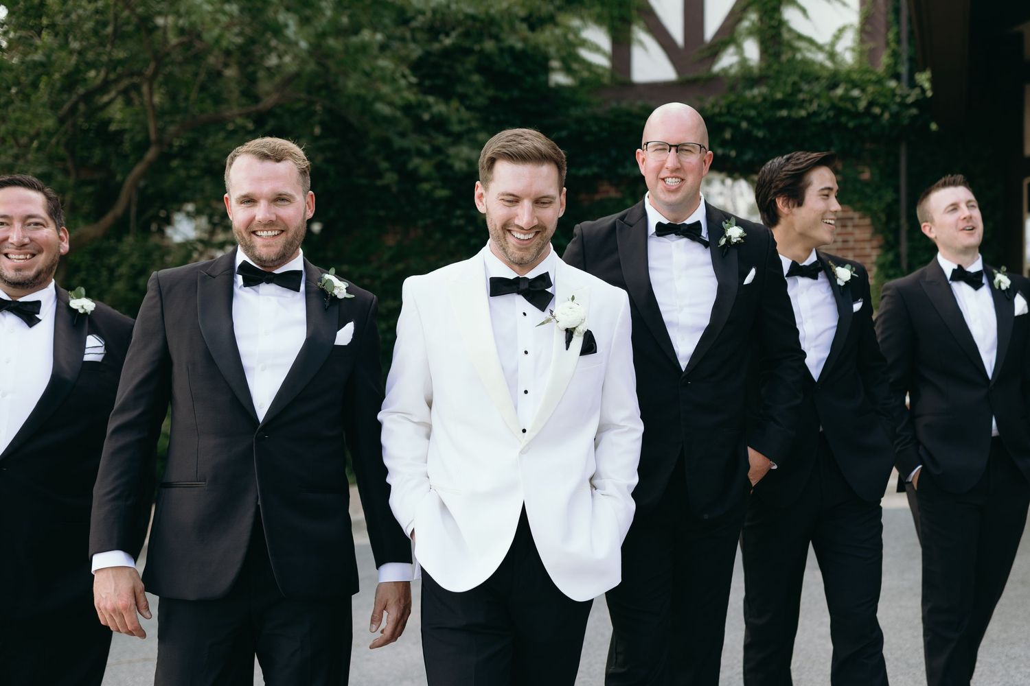 Groomsmen in formal black and white tuxedos standing together at an elegant wedding celebration.