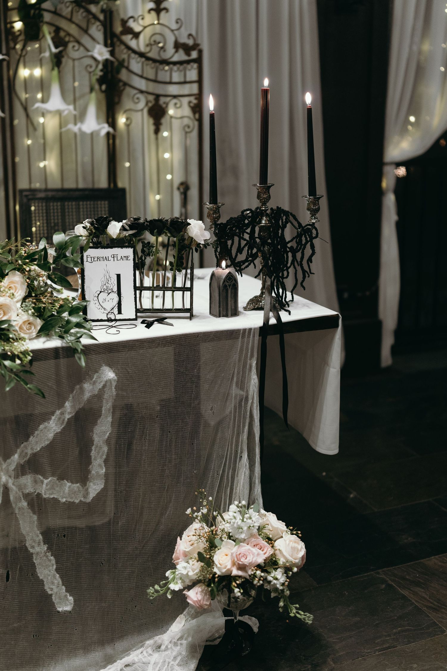 Wedding decor featuring black candelabras, floral arrangements, and romantic lighting on a draped table.