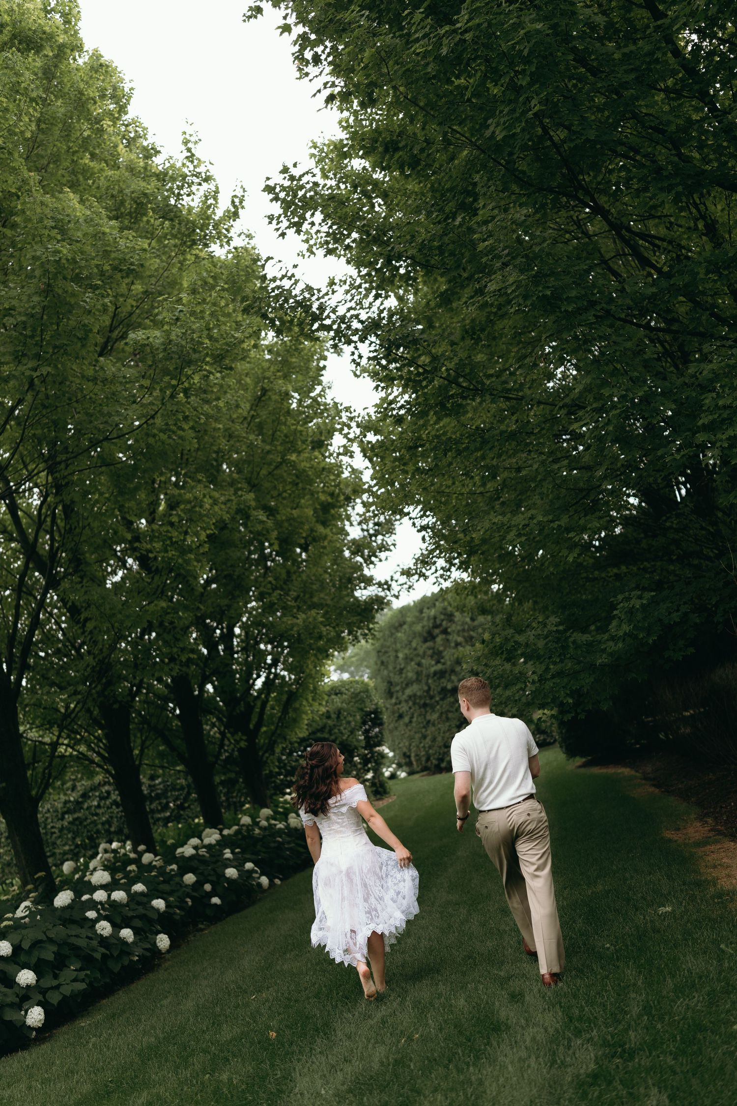 A couple walks hand in hand down a tree-lined garden path with blooming hydrangeas. The Villa Terrace Milwaukee