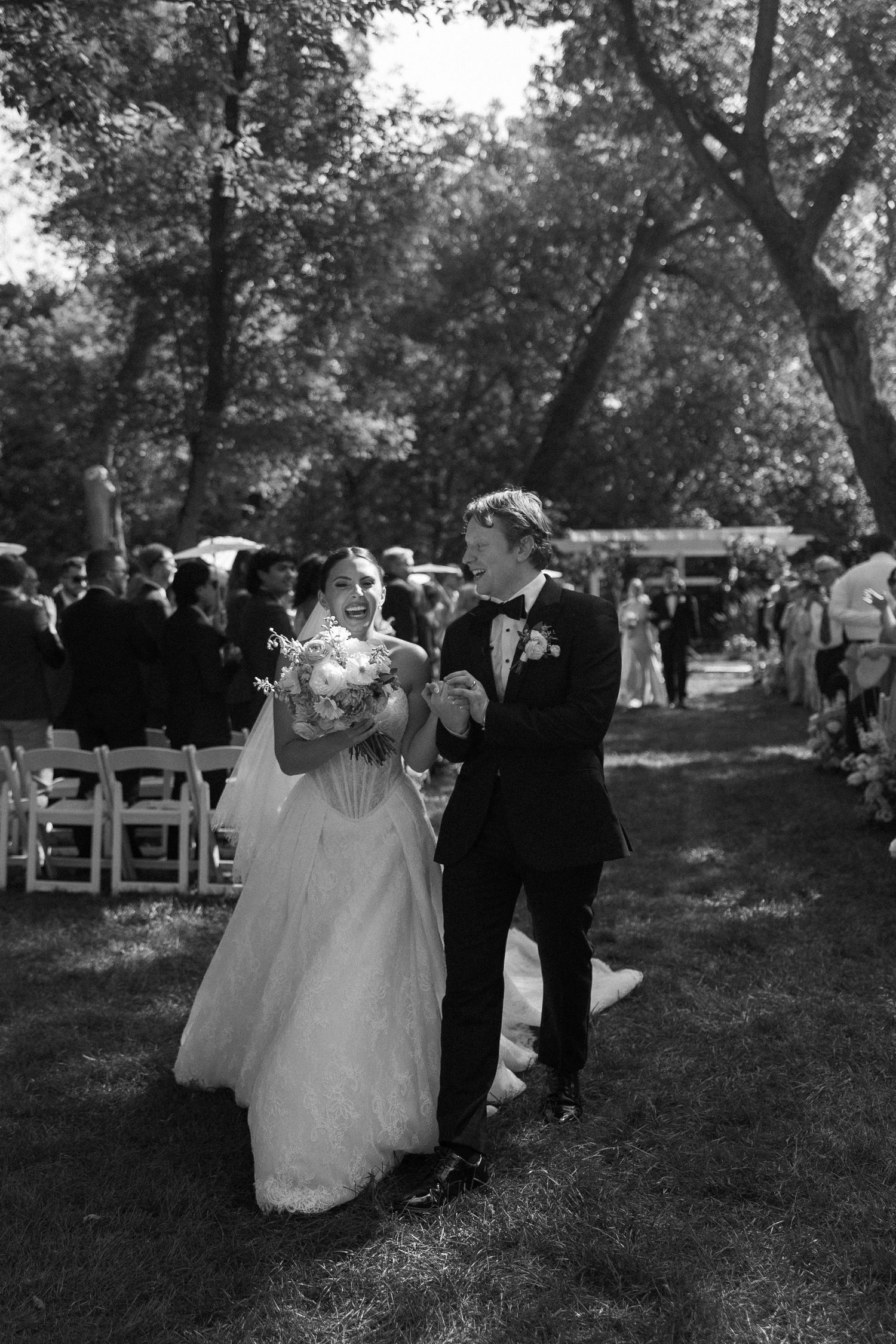 Black and white photo of a joyful bride and groom walking down the aisle at an outdoor wedding ceremony.