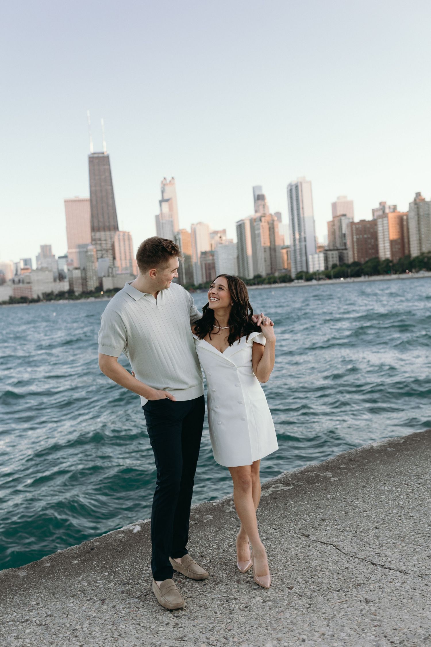 A couple shares a romantic moment along Lake Michigan with Chicago's skyline creating a stunning backdrop at sunset.