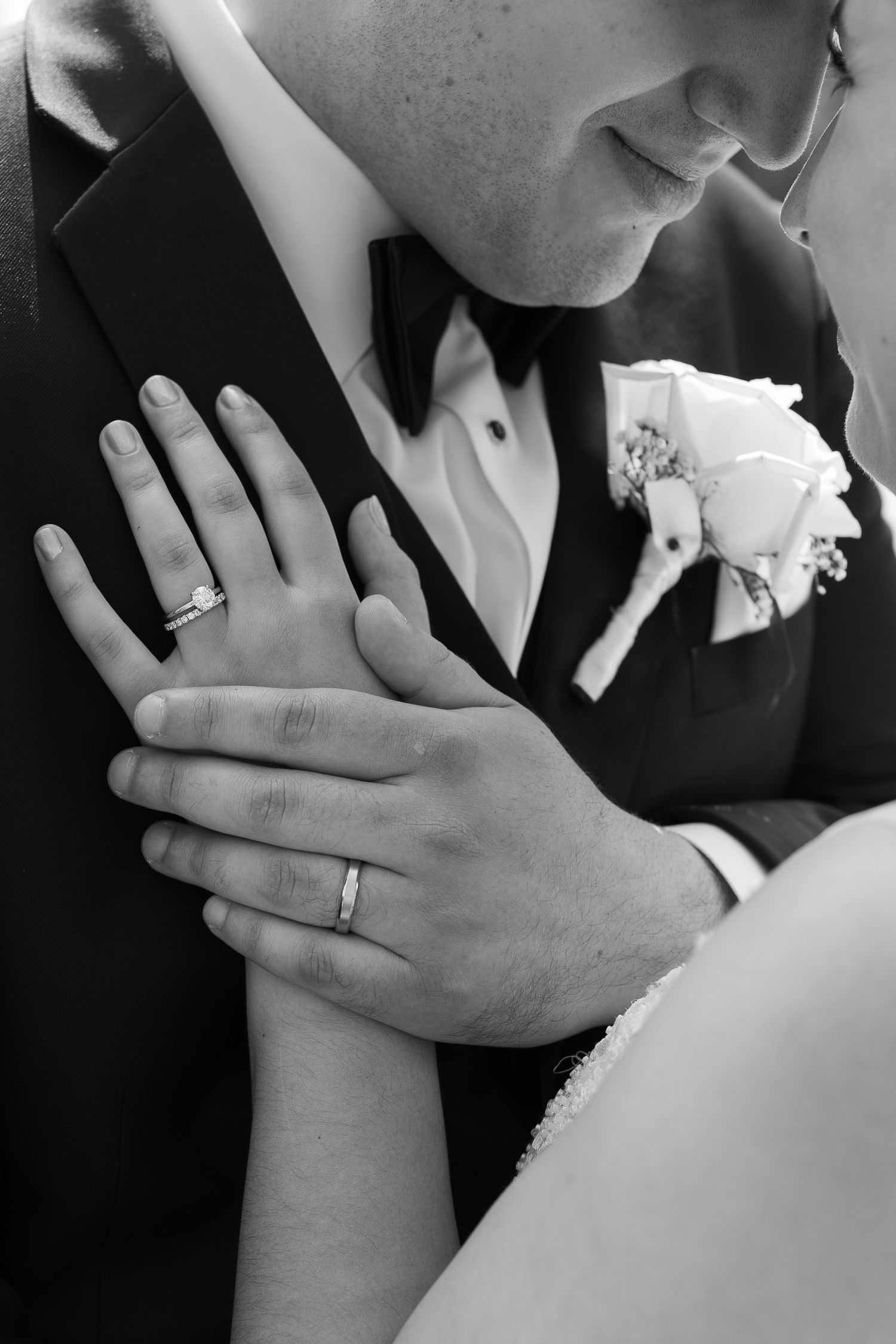 Close up of wedding rings and hands with white rose boutonniere.