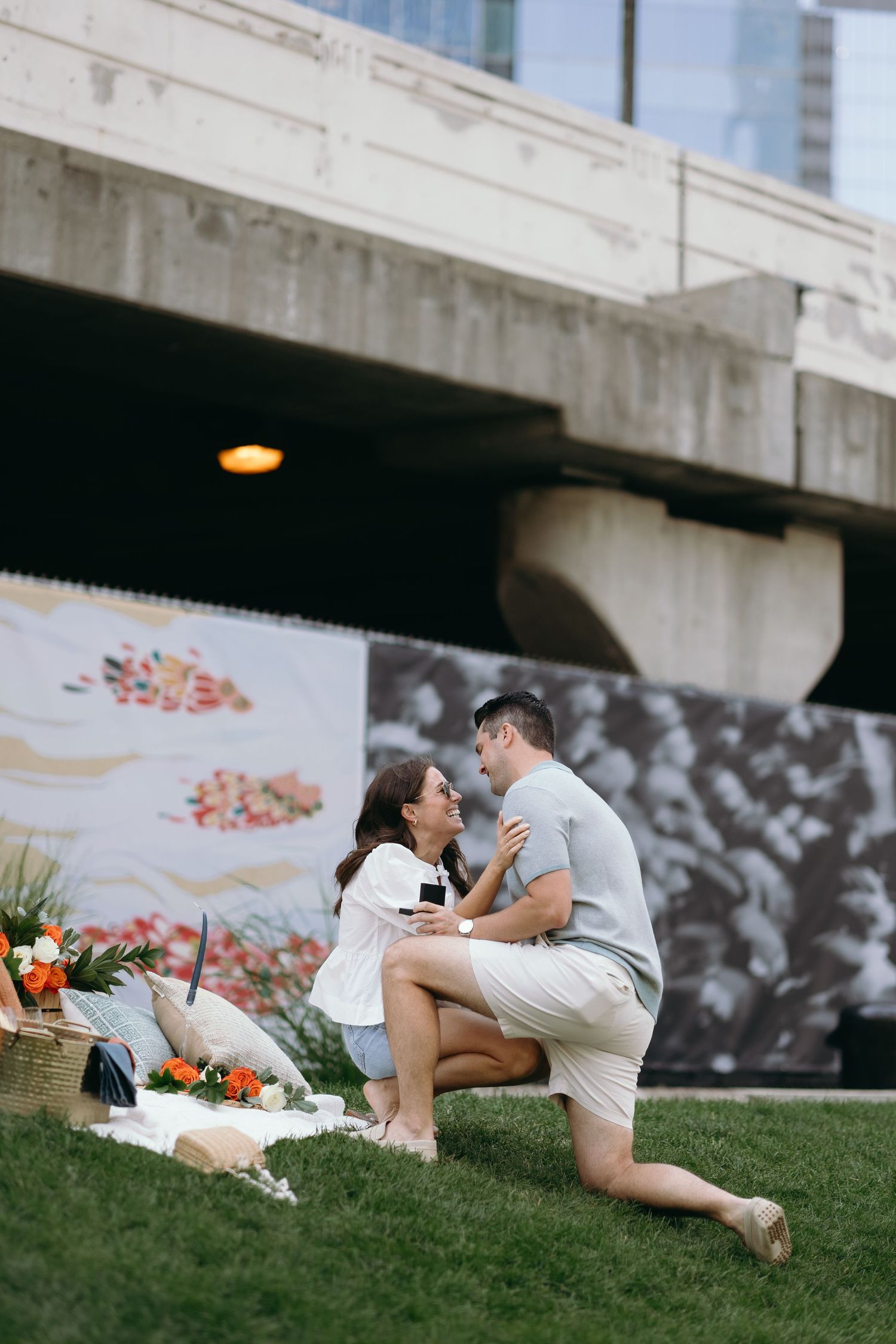 A couple shares an intimate moment while laying on a grassy slope against a white concrete building.