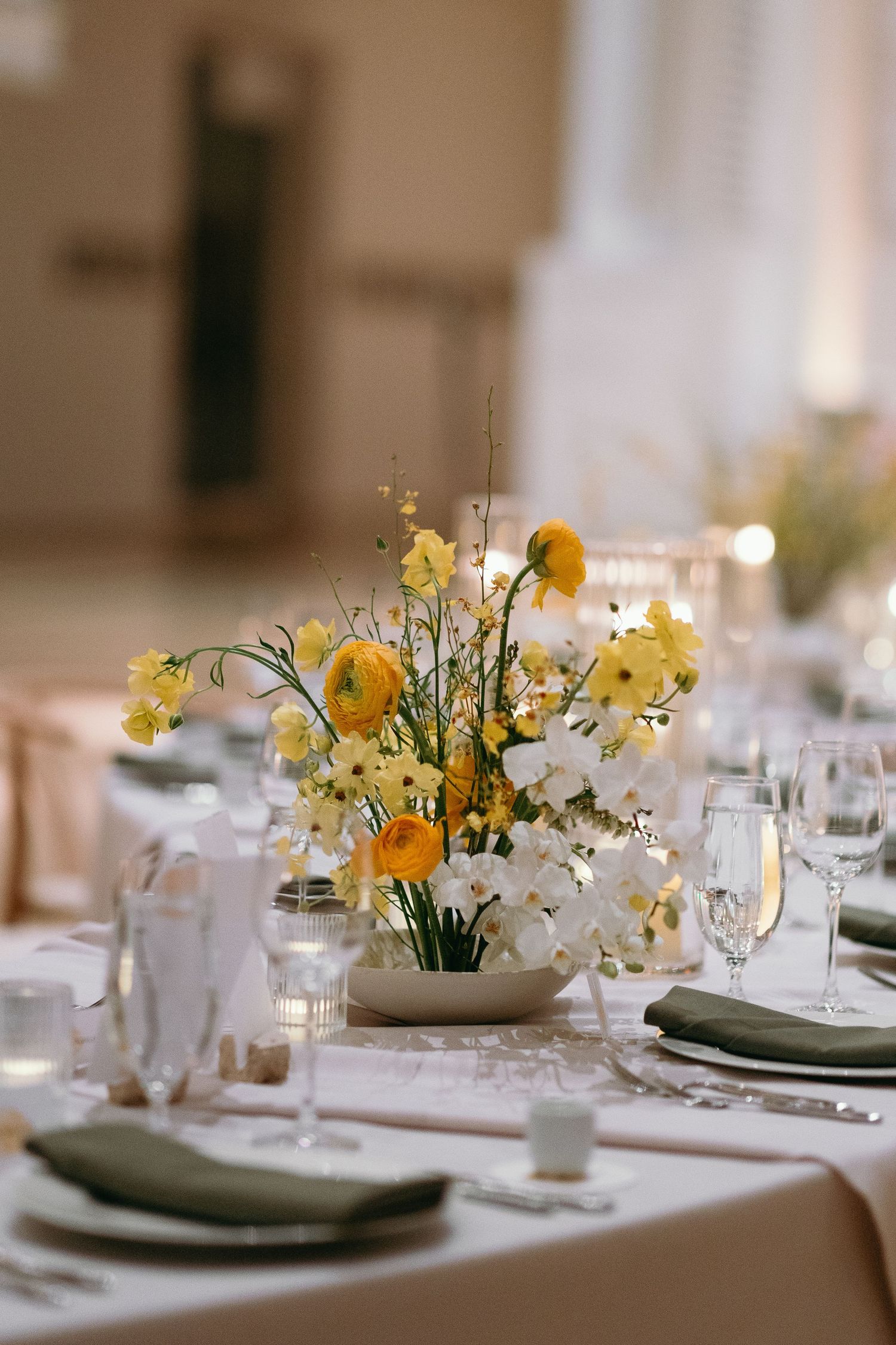 Yellow and white floral centerpiece on an elegantly set wedding reception table.