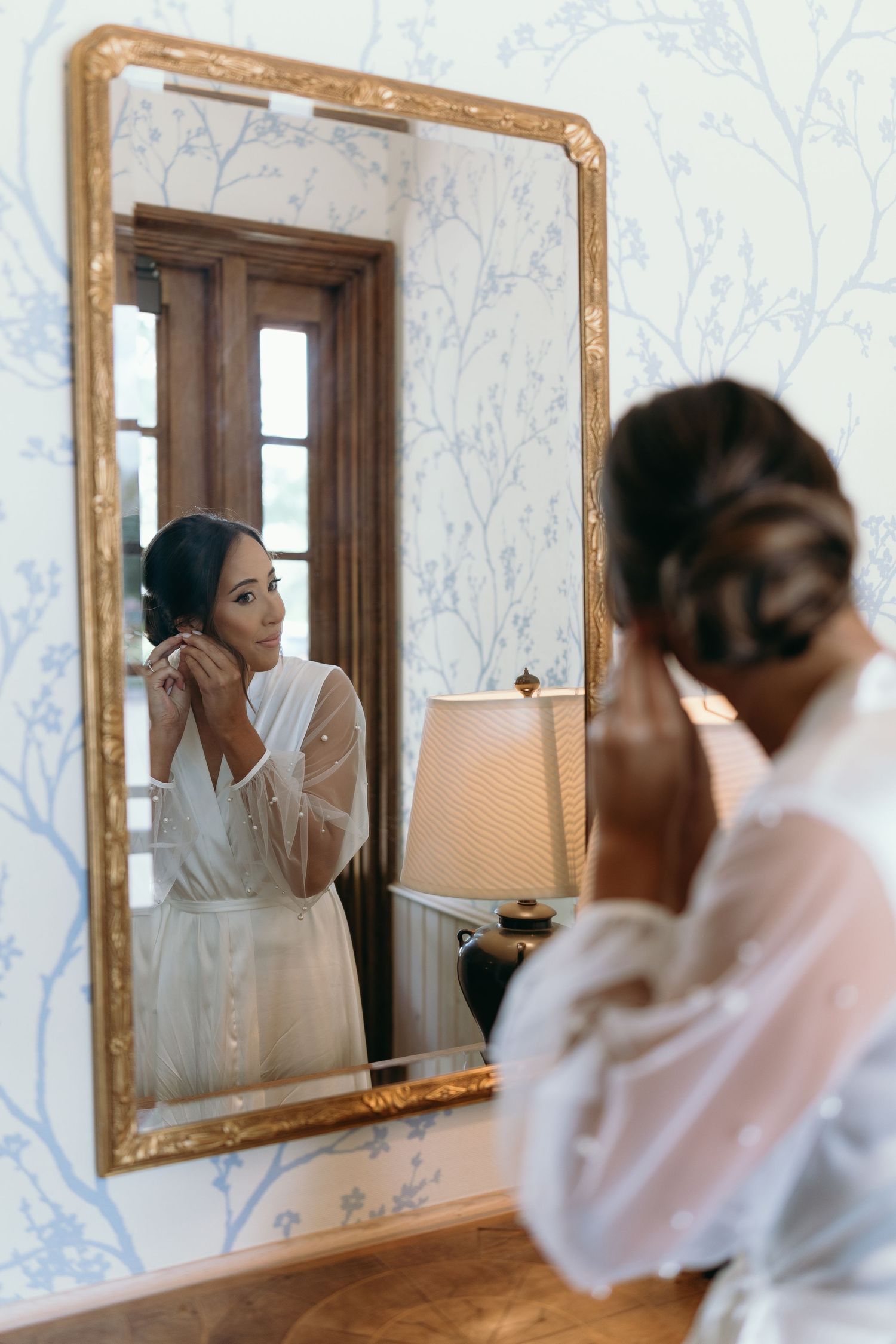 Elegant wedding preparation scene with gold-framed mirrors and floral wallpaper.