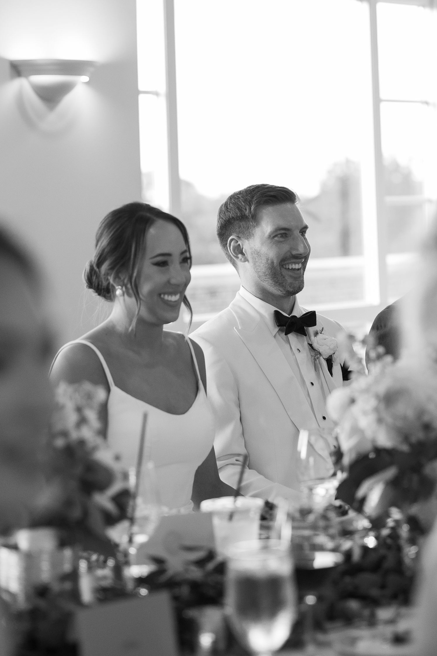 Happy newlyweds smiling together at their reception table with elegant floral decor.