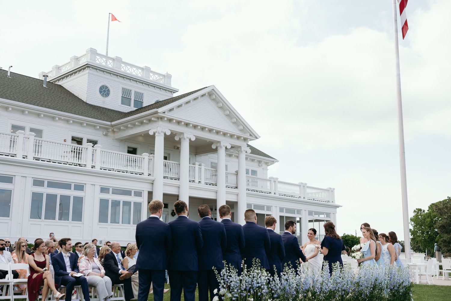 Elegant outdoor wedding ceremony at a grand white mansion with columns and coastal architecture.