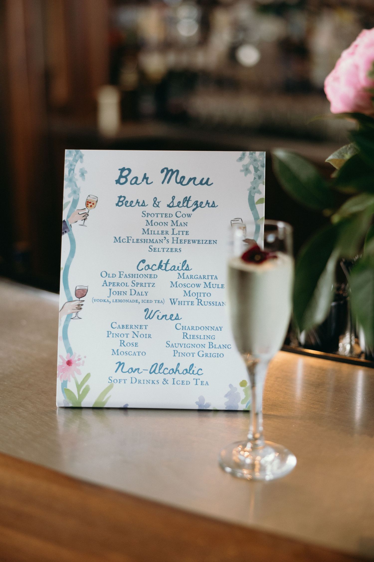 Bar menu card with floral design and wine glass sitting on wooden surface at restaurant or event venue.