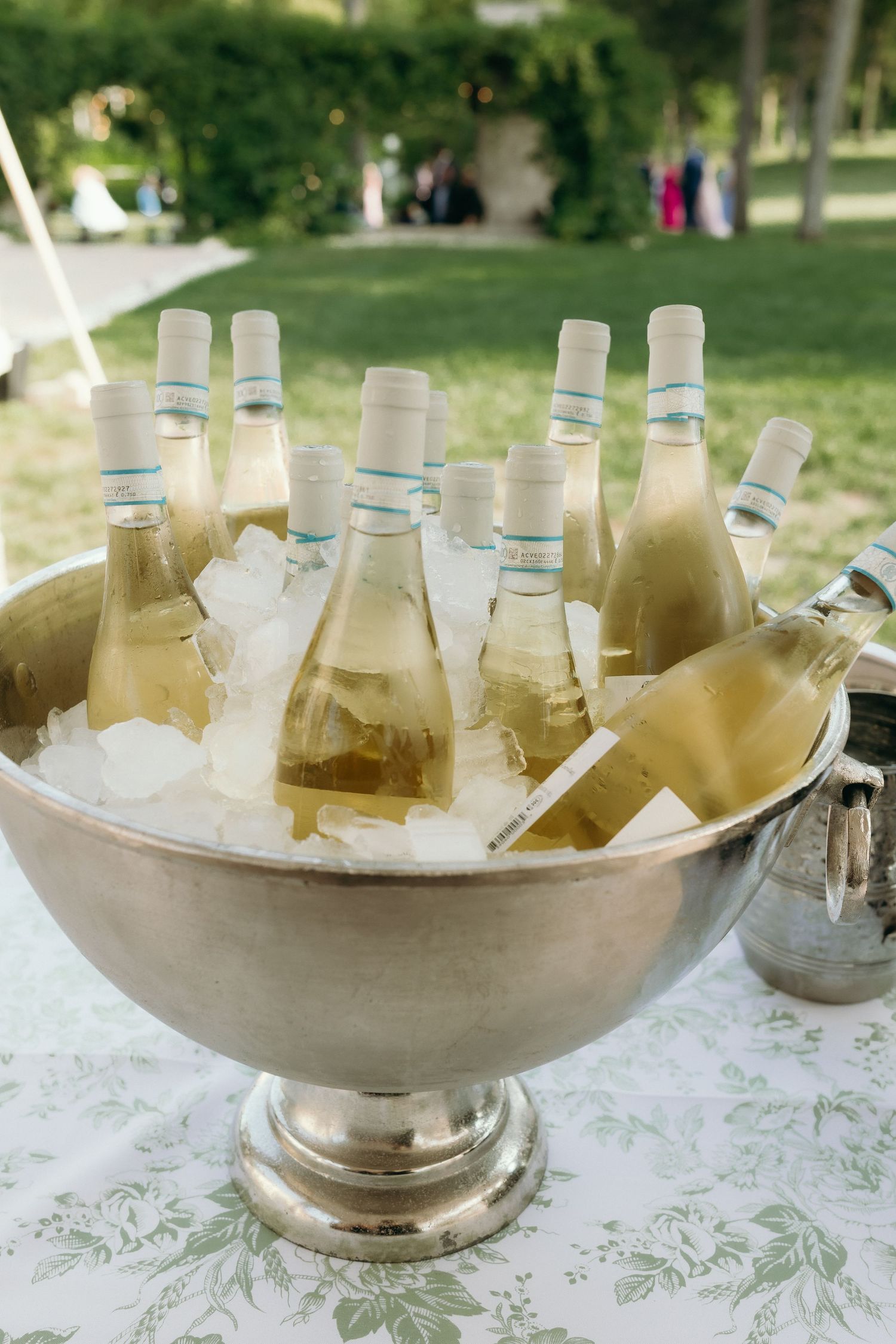 Multiple chilled white wine bottles arranged in a large silver ice bucket at an outdoor wedding.