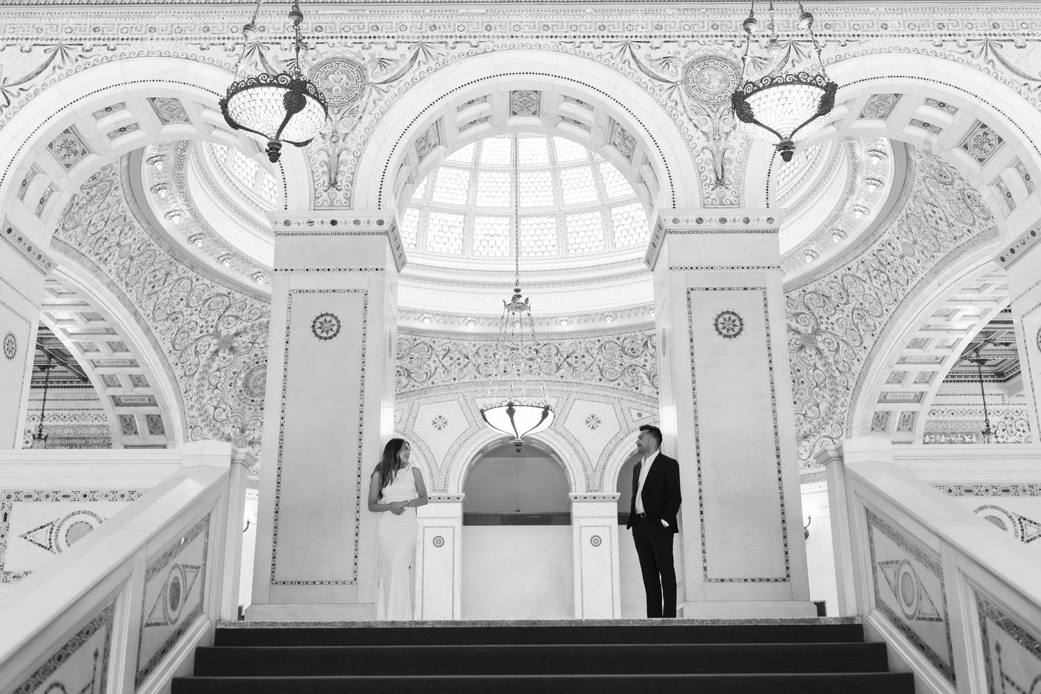 Couple stands apart on elegant marble staircase with ornate architectural details. Cultural Center engagement photos