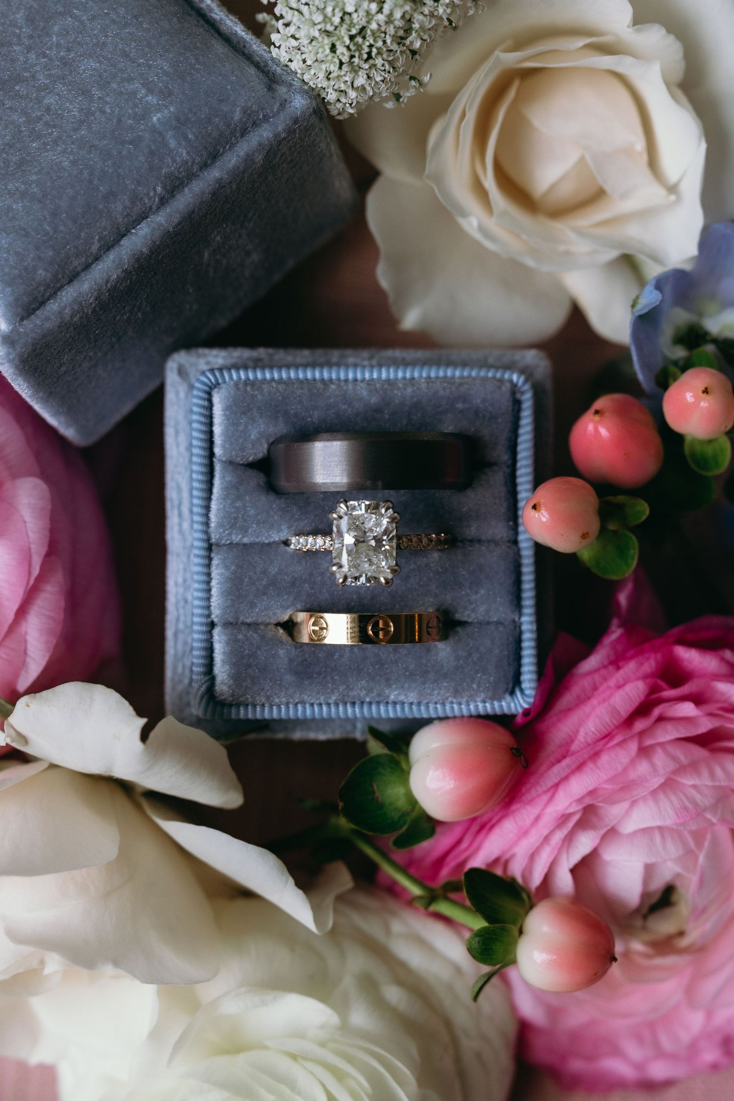 Wedding rings nestled in blue velvet boxes surrounded by pink and white flowers.