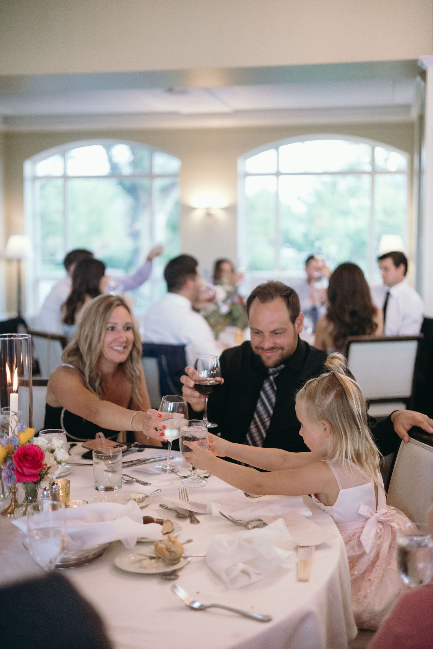 Family enjoying dinner together at an elegant wedding reception with large windows.