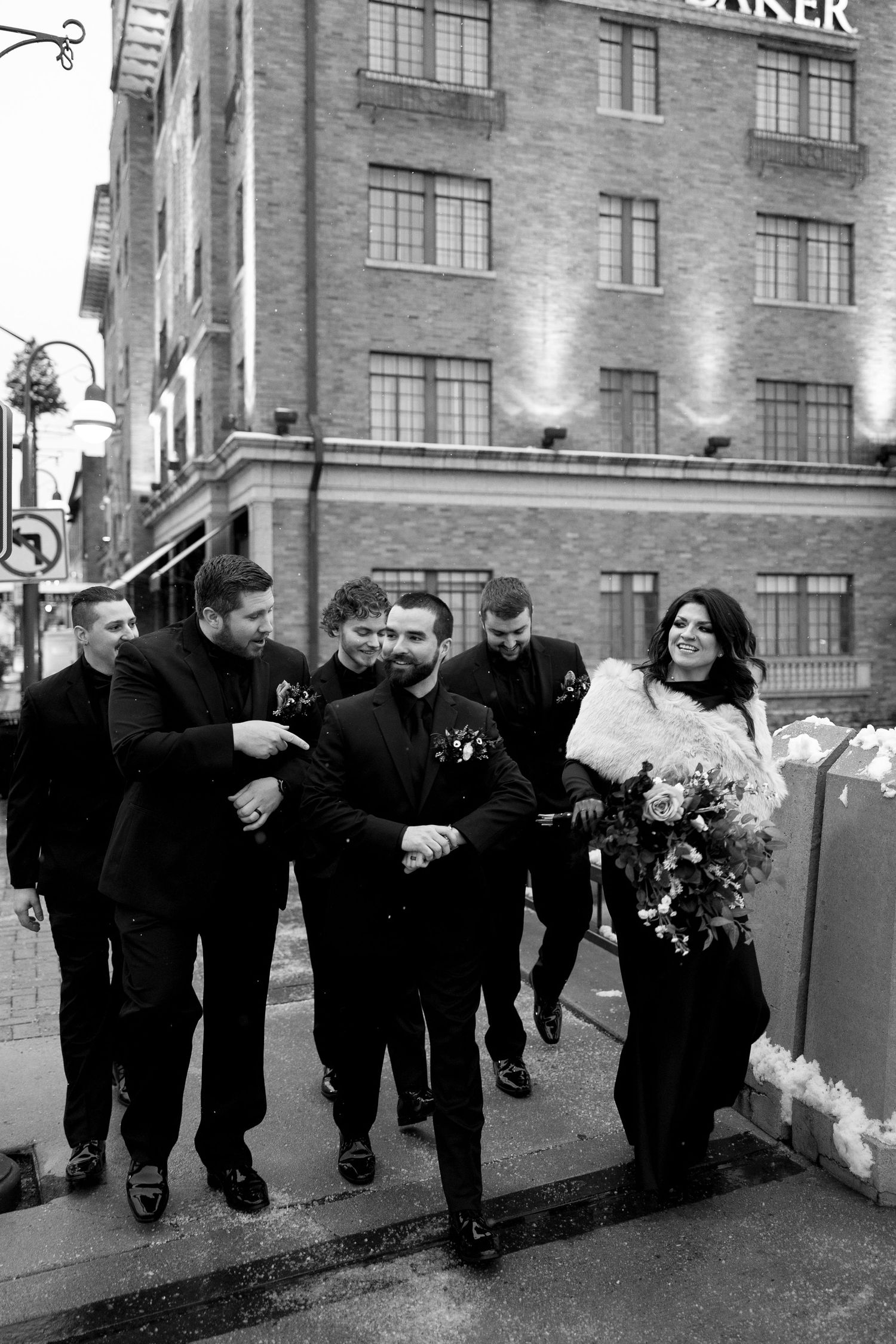 Wedding party walking outside brick building in black and white formal attire.
