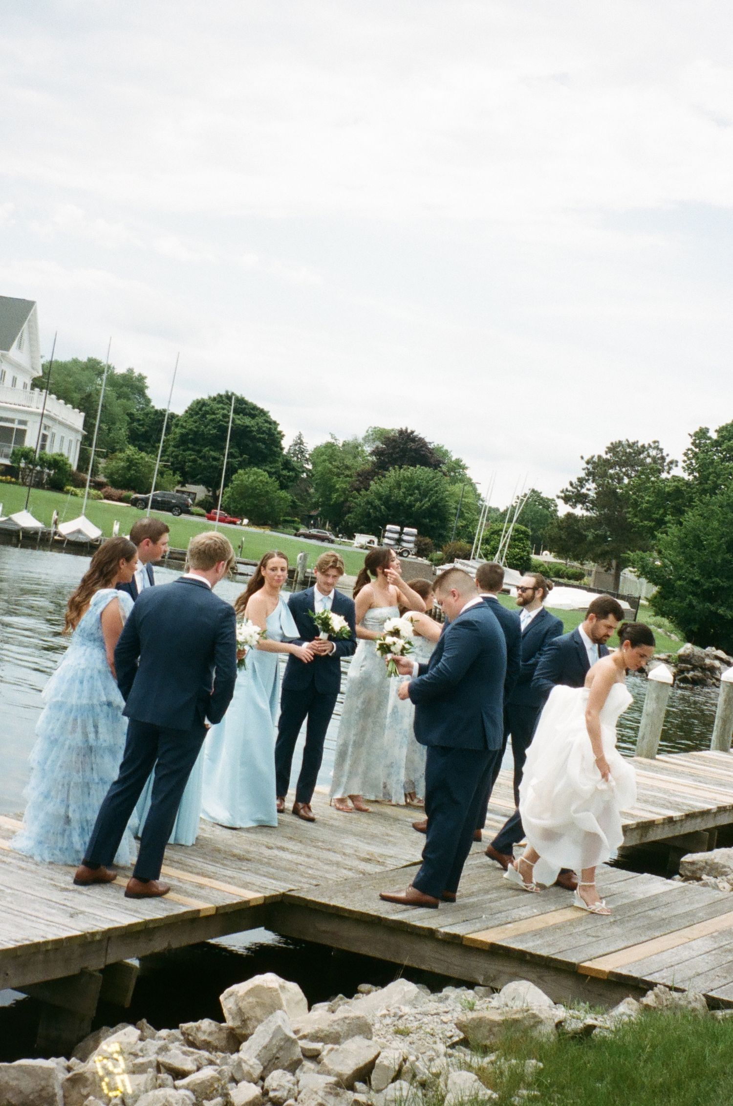 Wedding party gathered on wooden dock by waterfront during daytime celebration.