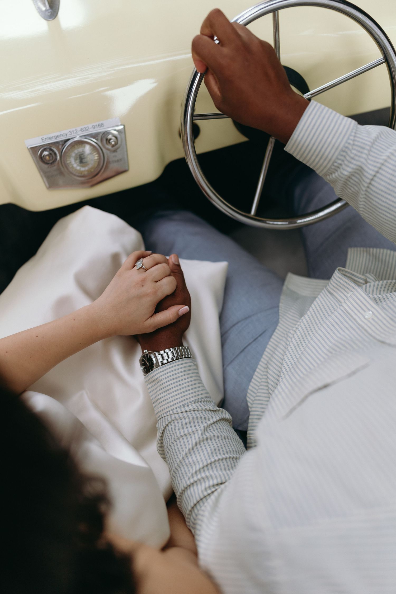 Couple holding hands in a vintage car, man wearing a watch and ring, woman in white dress, romantic wedding scene.
