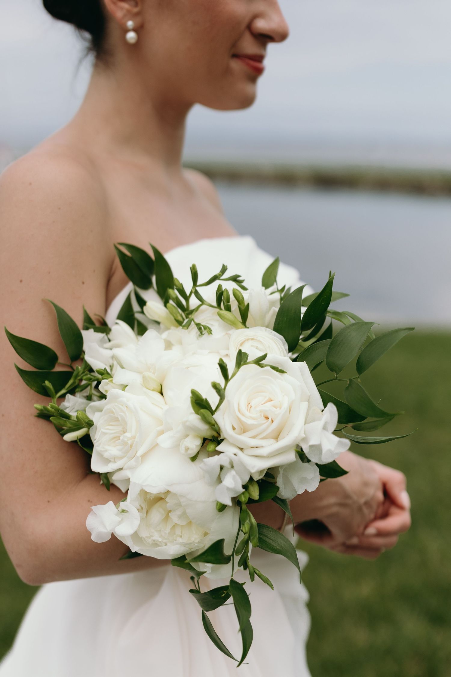 A series of white floral bridal bouquets featuring roses and greenery held against a natural outdoor background.